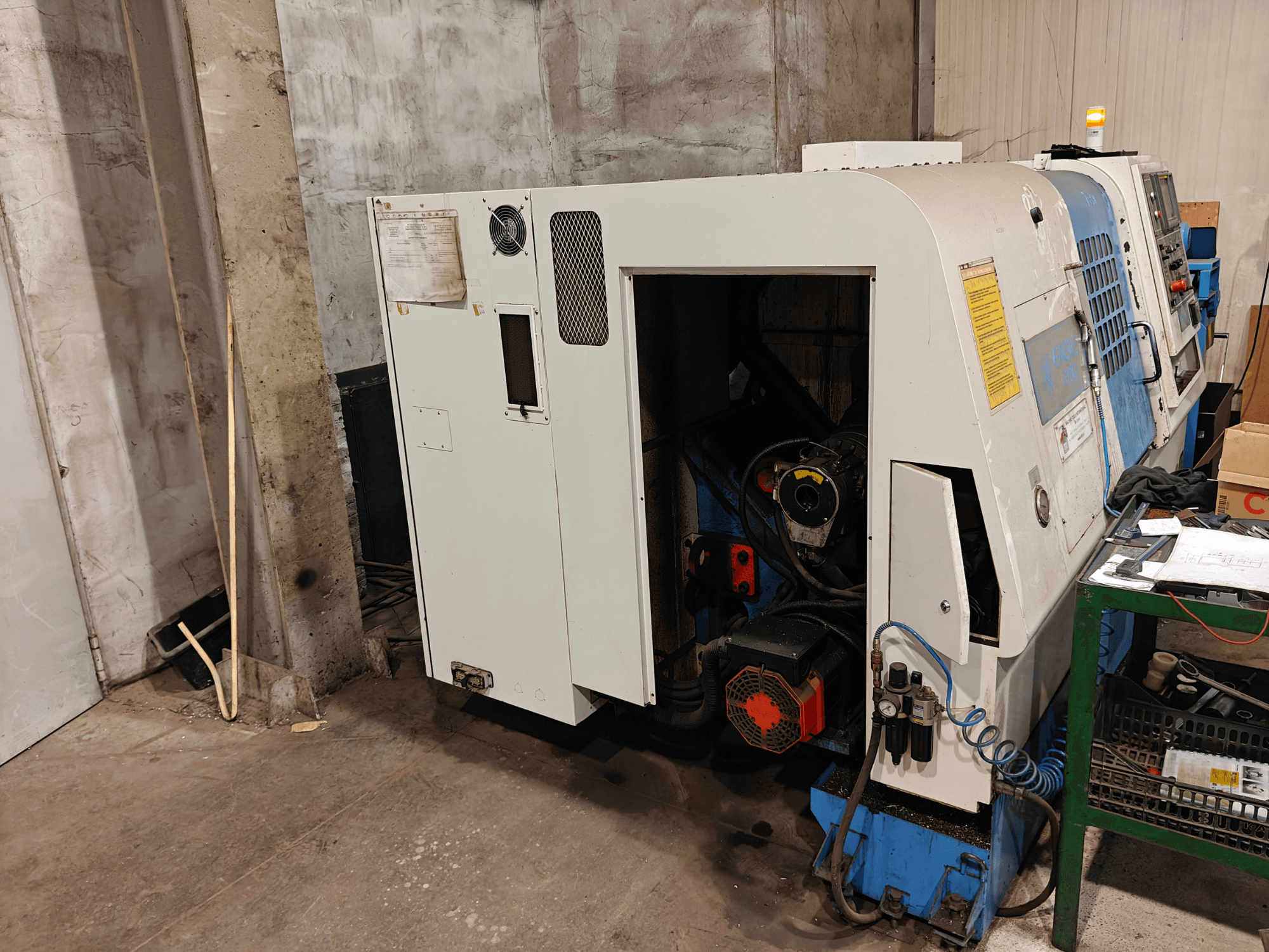 Вид спереду токарного верстата, марка та модель не вказані, з елементами керування та видимими компонентами двигуна.