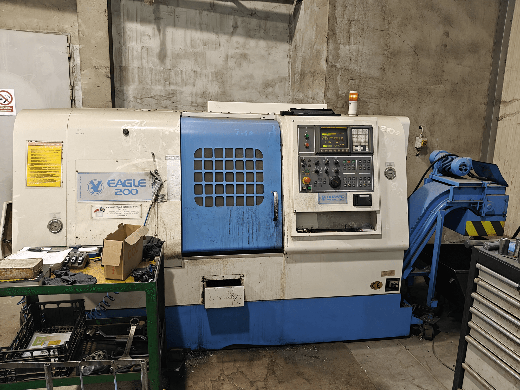 Верстат з ЧПУ Eagle 200, вид спереду з панеллю керування, різні інструменти на зеленому візку. Видимий знос і робочі індикатори.