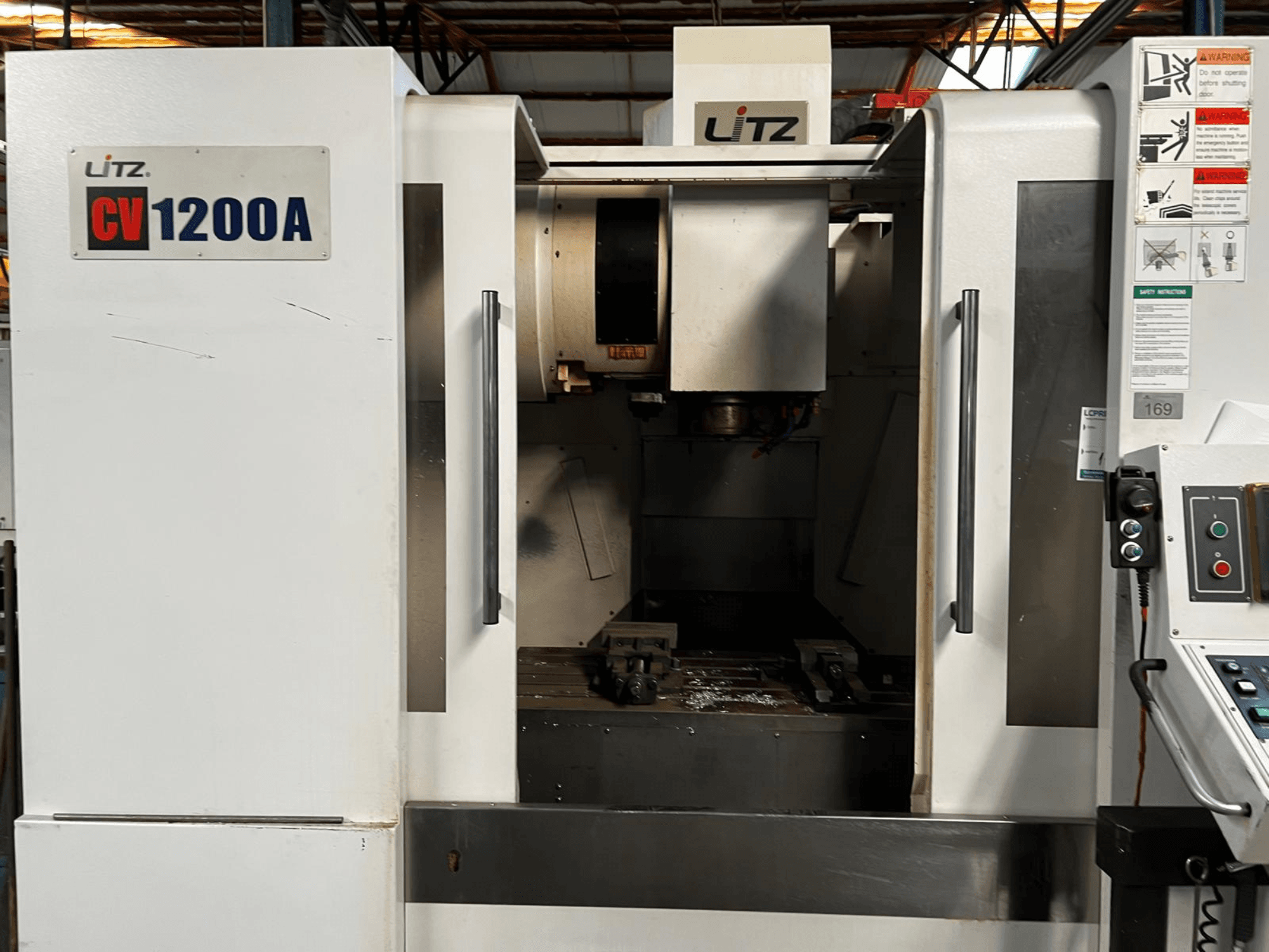 Вертикальний обробний центр Litz CV1200A, вид спереду, на якому видно панель управління, шпиндель та відкриті дверцята, що відкривають огляд робочої зони.