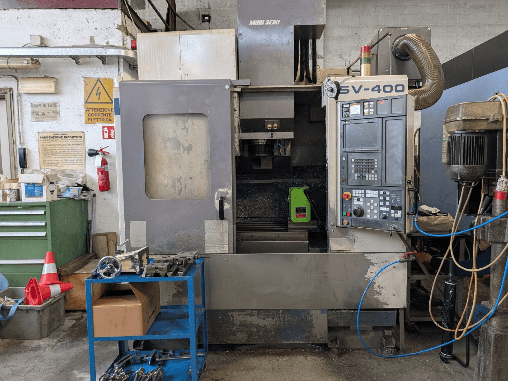 Вертикальний обробний центр MORI SEIKI SV-400 у майстерні, вид збоку, демонстраційна панель керування та верстати поруч.