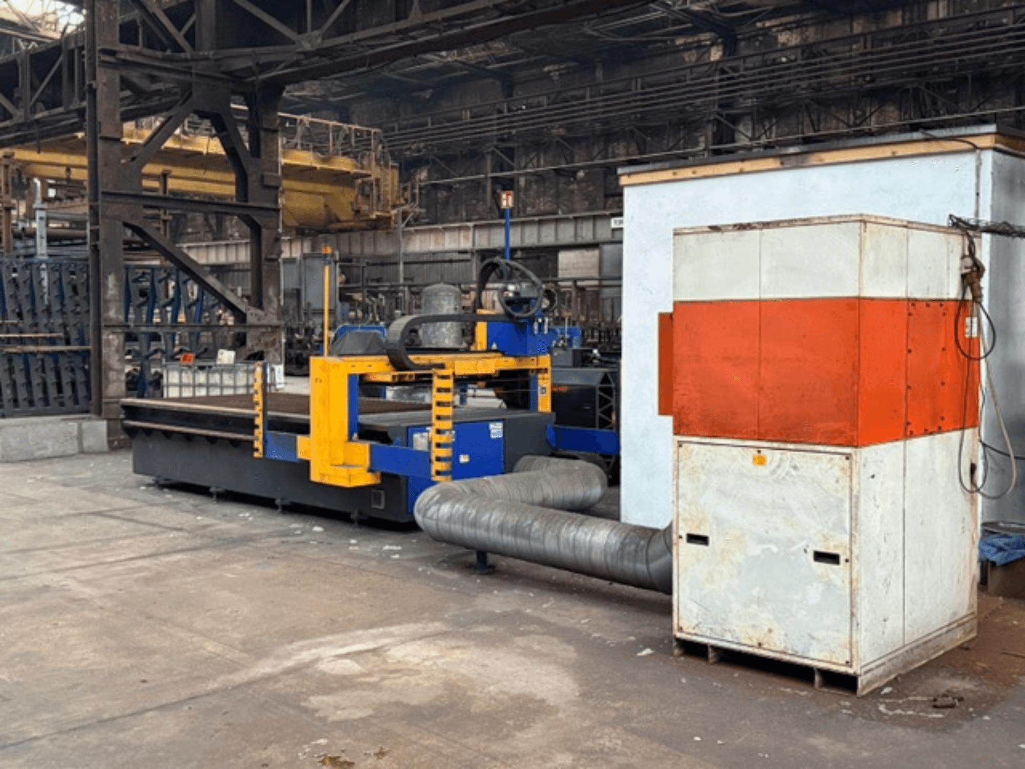 Машина для плазмового різання MicroStep 3001.15P/ME у заводських умовах, вид збоку, з жовтими та синіми компонентами та приєднаною витяжною системою.
