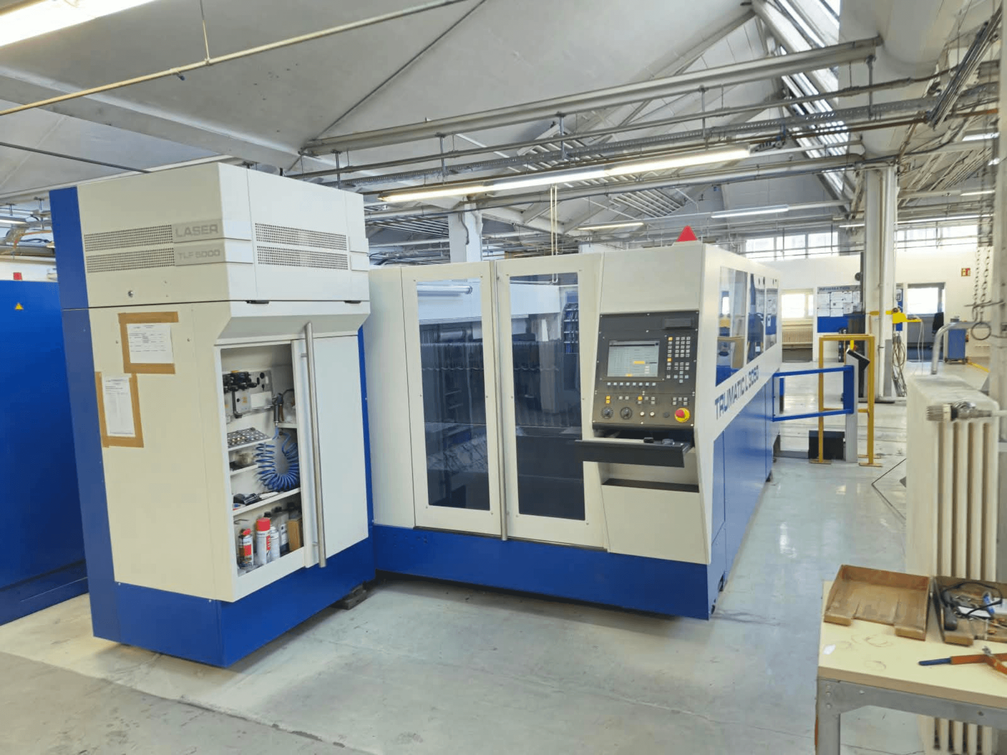 Лазерний верстат для різання CO2 TRUMPF TruLaser L3050, вид спереду, з панеллю керування та дверцятами для доступу з метою технічного обслуговування, у заводській комплектації.