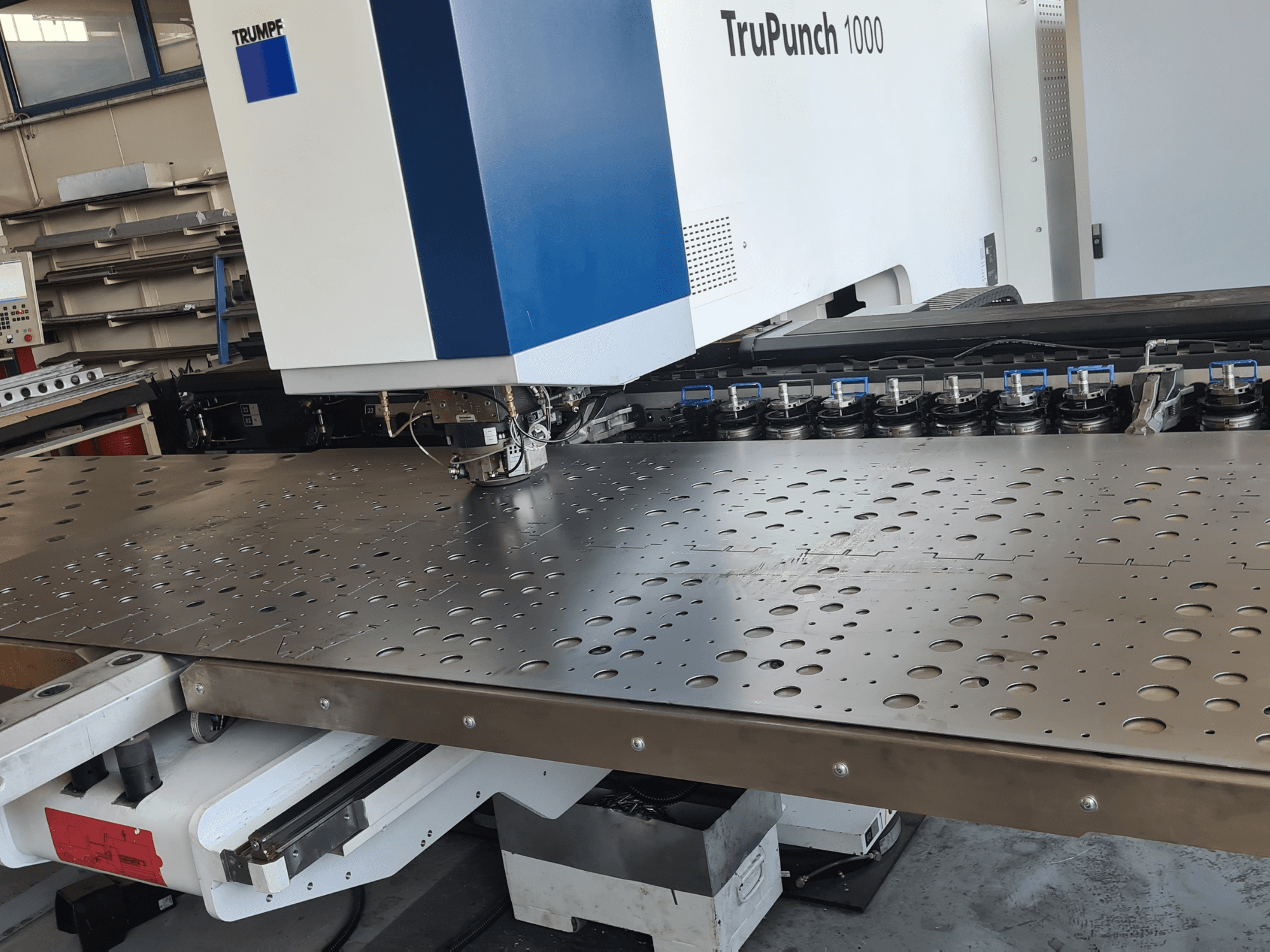 Штампувальний верстат з ЧПУ TRUMPF TruPunch 1000, вид спереду, на якому показано перфорований металевий лист та набір інструментів.