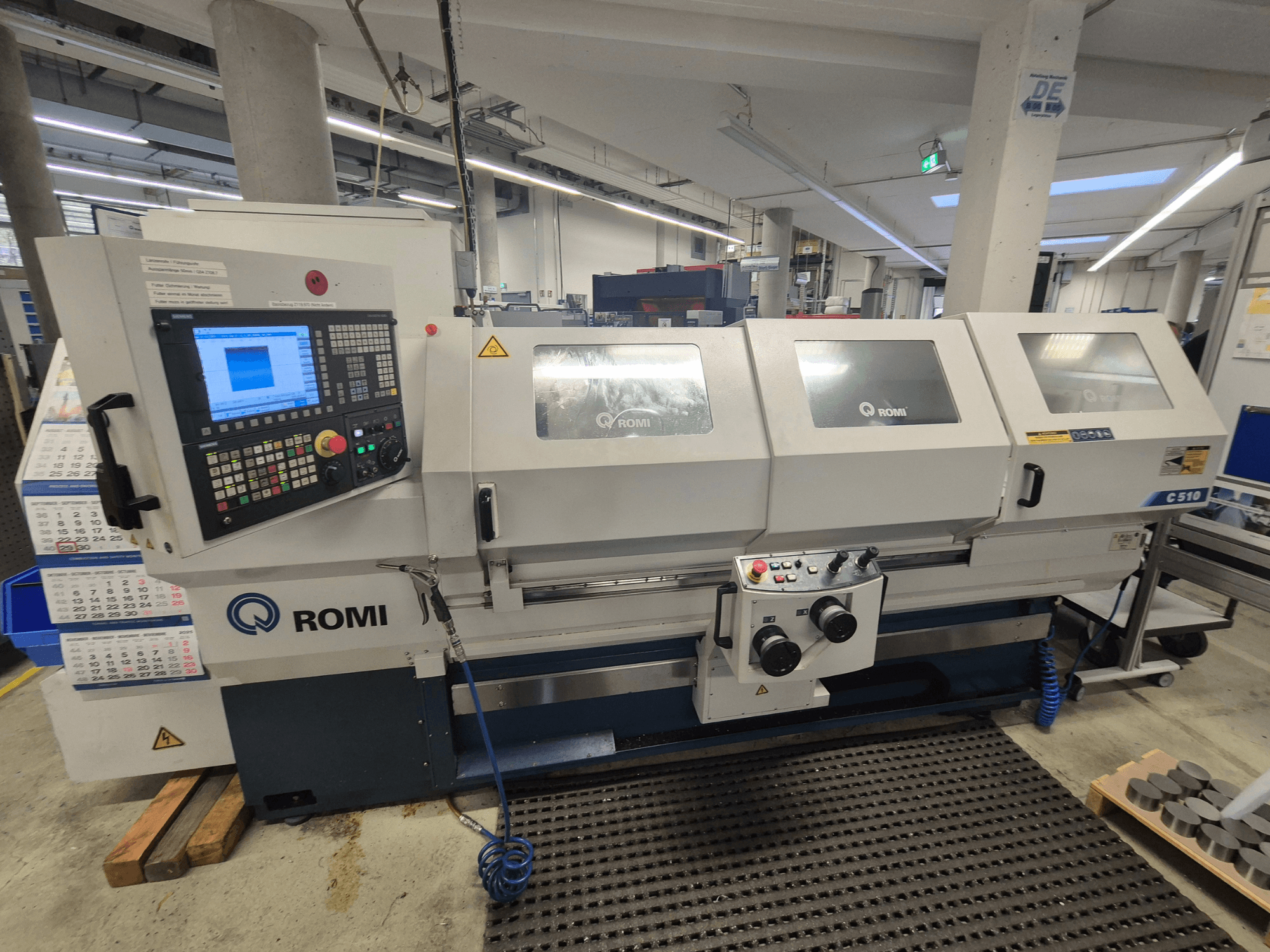 Токарний верстат Romi C510 спереду, з цифровою панеллю керування та трьома захисними кришками. Включає в себе попереджувальні етикетки з техніки безпеки.