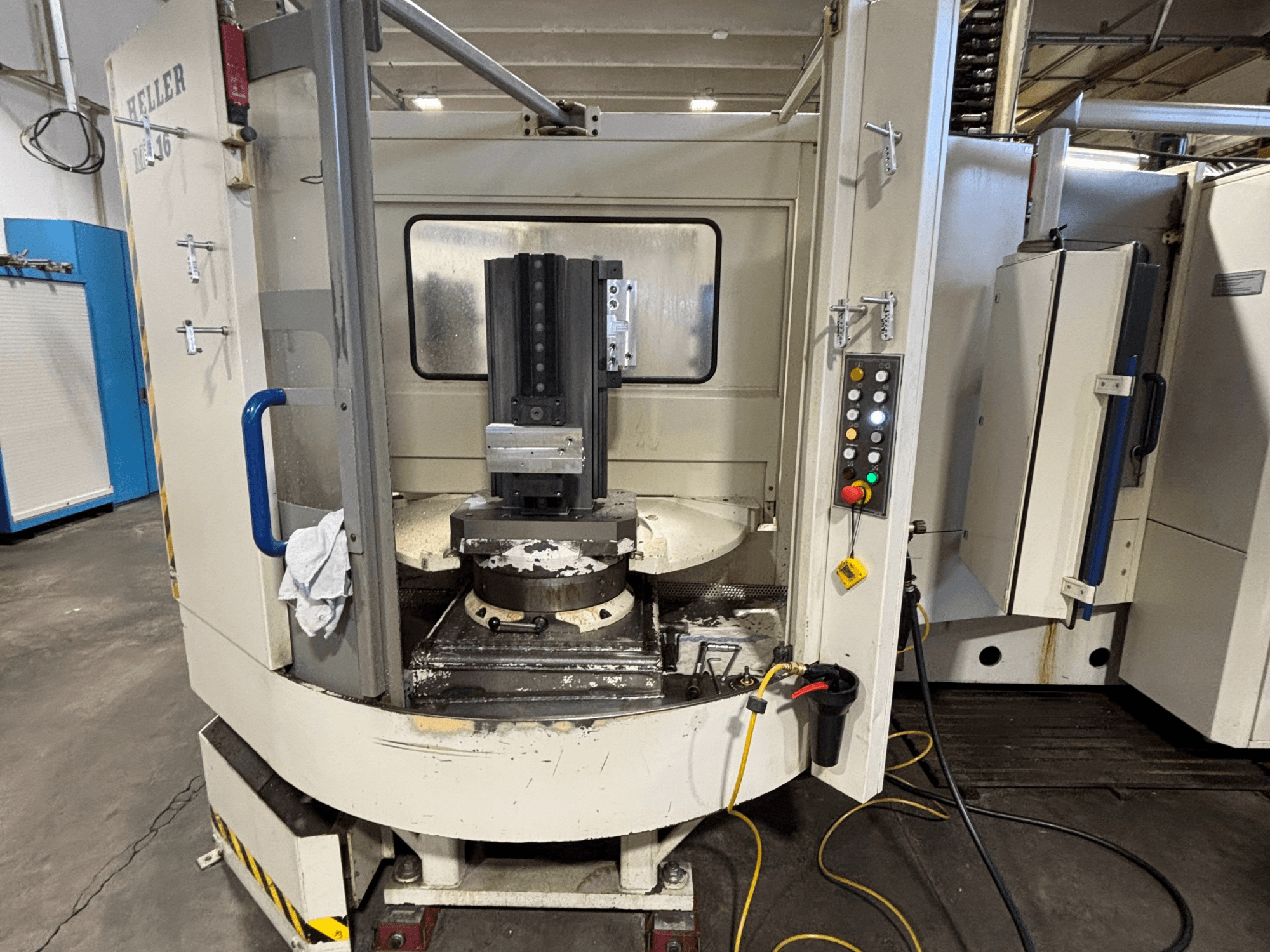 Обробний центр Heller, модель вертикальна, вид спереду: шпиндель, панель керування та робочий стіл з прикріпленим обладнанням.