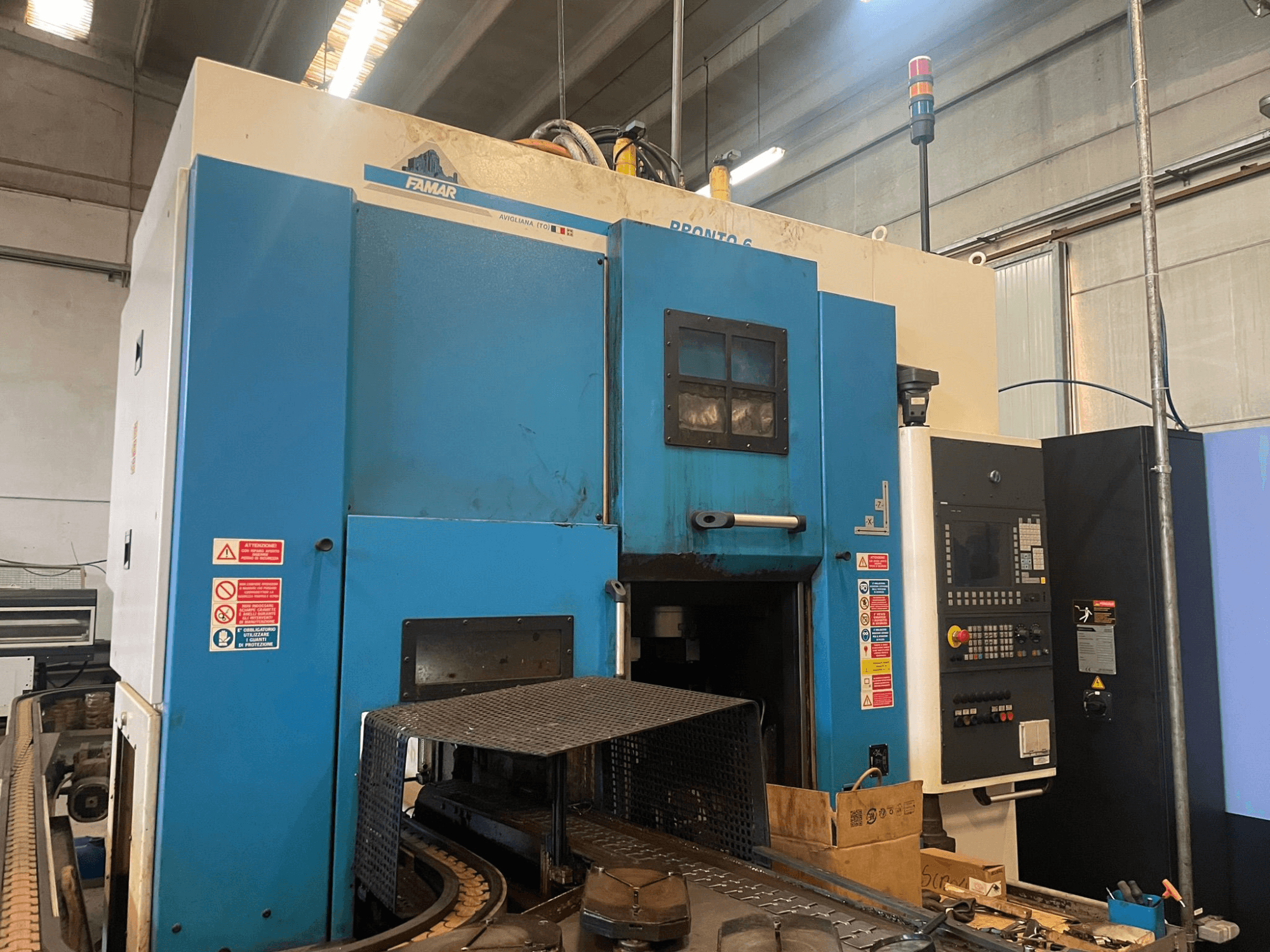 Вертикальний токарний верстат Famar Pronto 6 в майстерні, вид збоку, з панеллю керування, робочими функціями та етикетками безпеки.