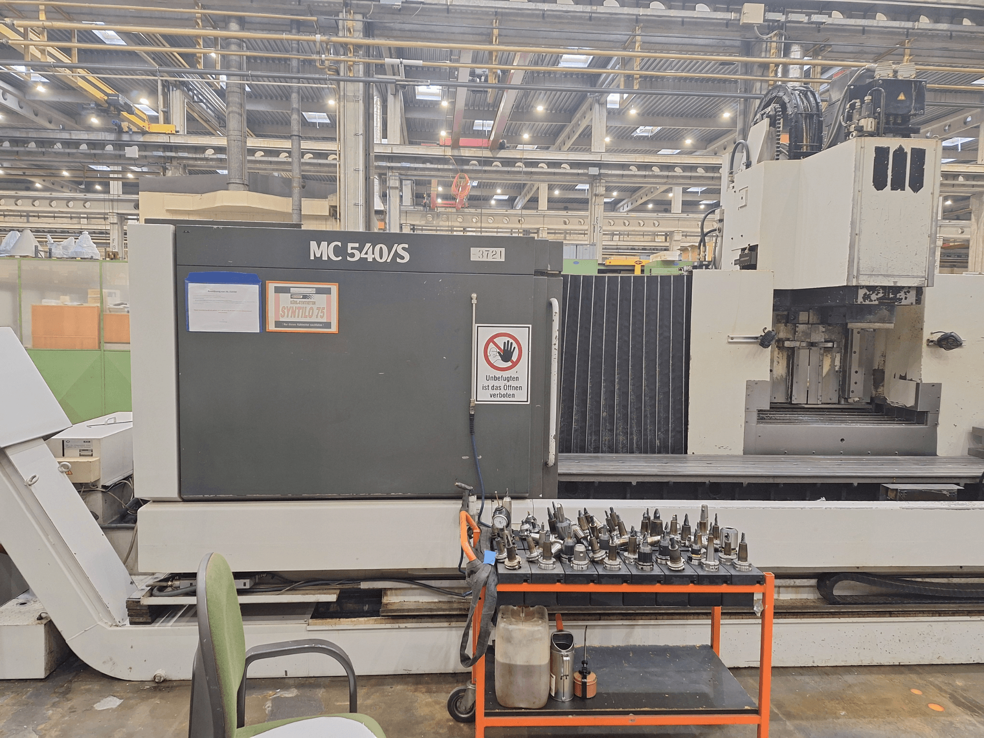 Вертикальний обробний центр STAMA MC 540S в майстерні, вид збоку з тримачами інструментів на візку поруч.