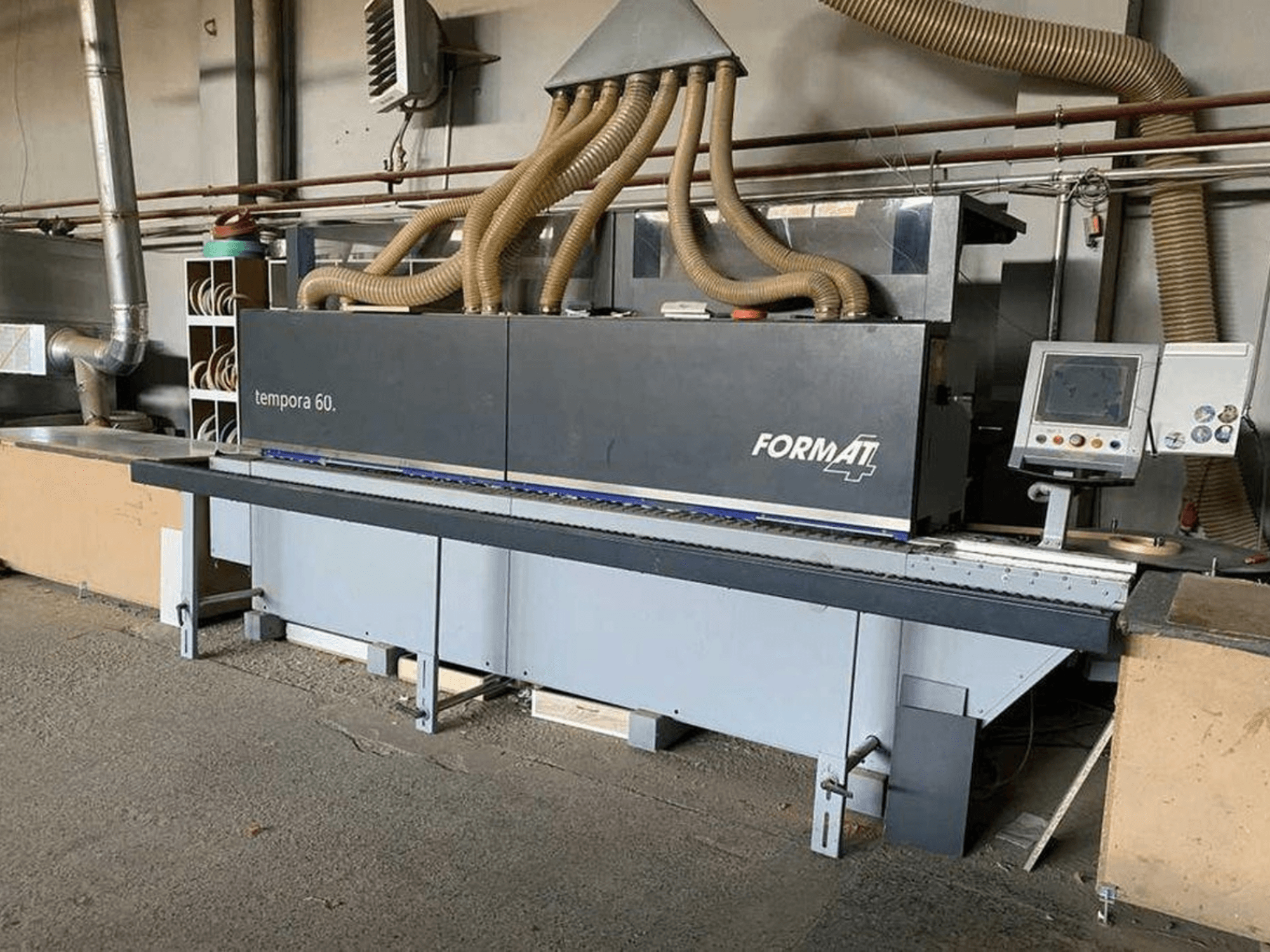 Кромкооблицювальний верстат FORMAT4 Tempora 60 у вигляді збоку, з декількома шлангами і панеллю керування з кнопками та екраном.