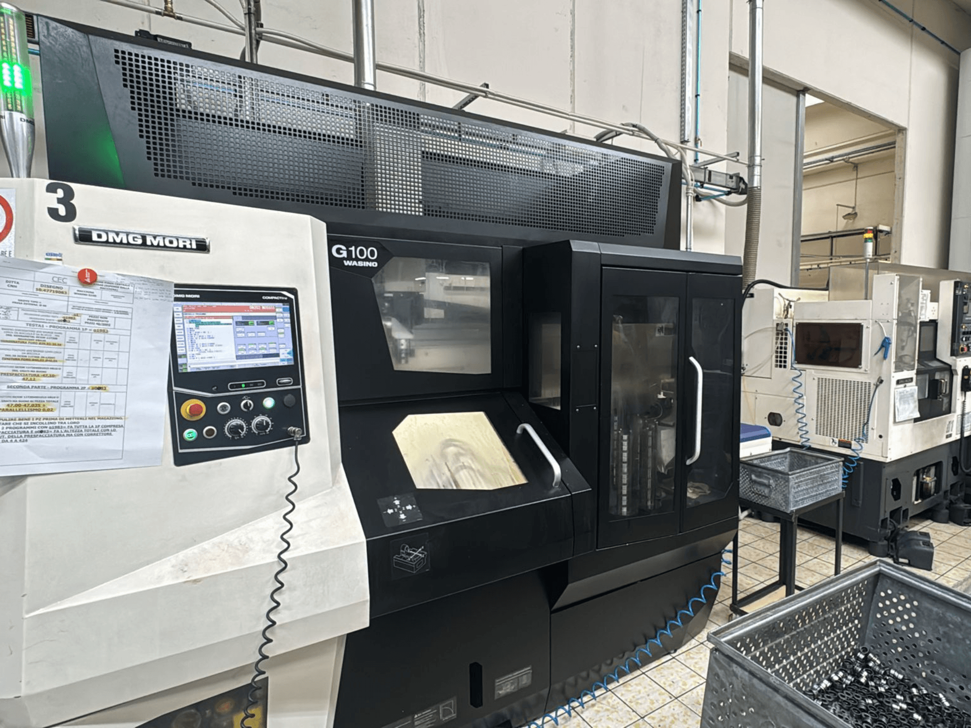 Верстат DMG MORI G100 на заводі, вид спереду, з цифровою панеллю керування та розташованими поруч контейнерами для зберігання інструментів.