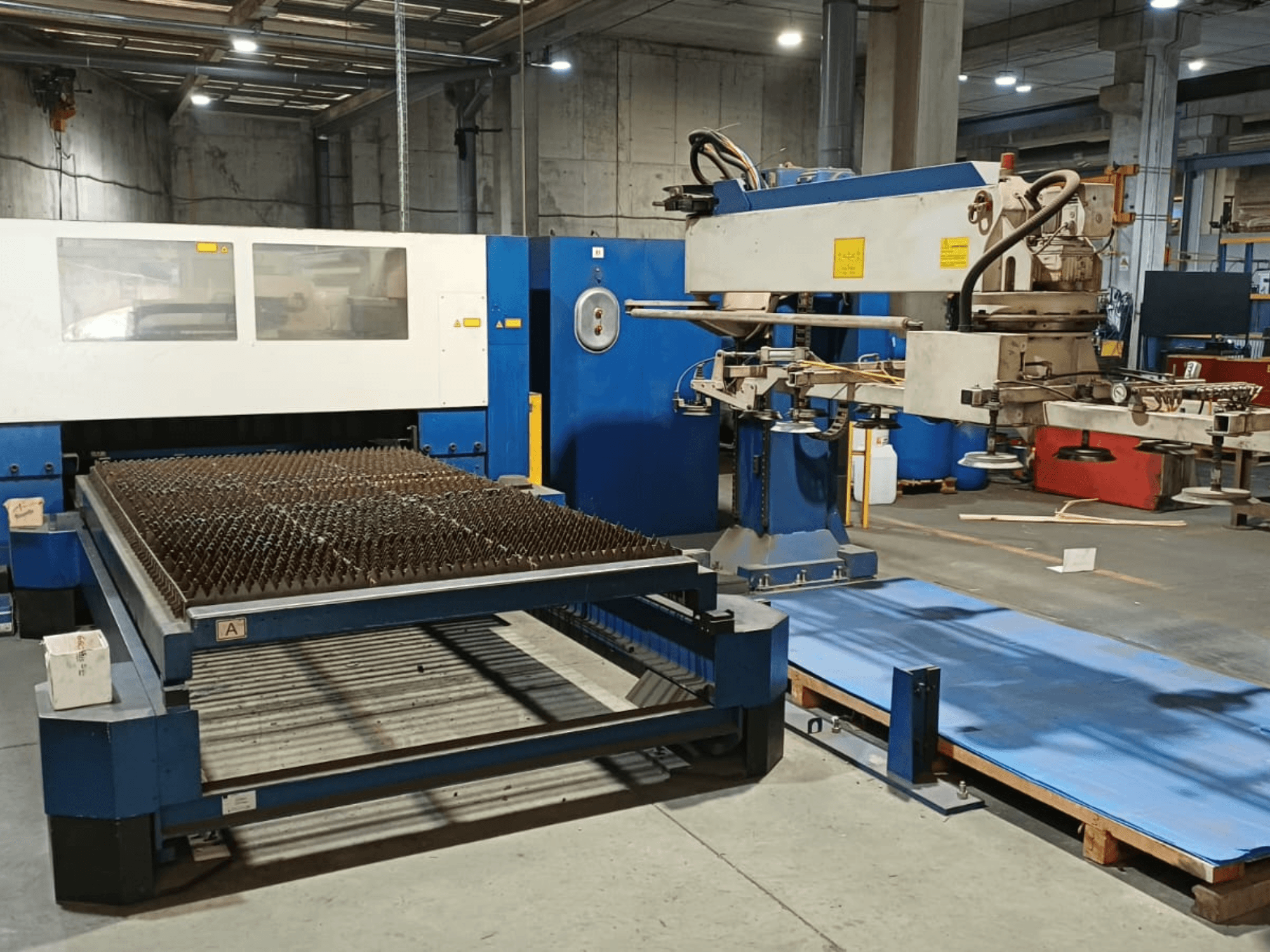 Лазерний верстат для різання CO2 TRUMPF TRUMATIC L 3030, вид збоку, на якому видно різальний стіл із рельєфною поверхнею та робочий маніпулятор.