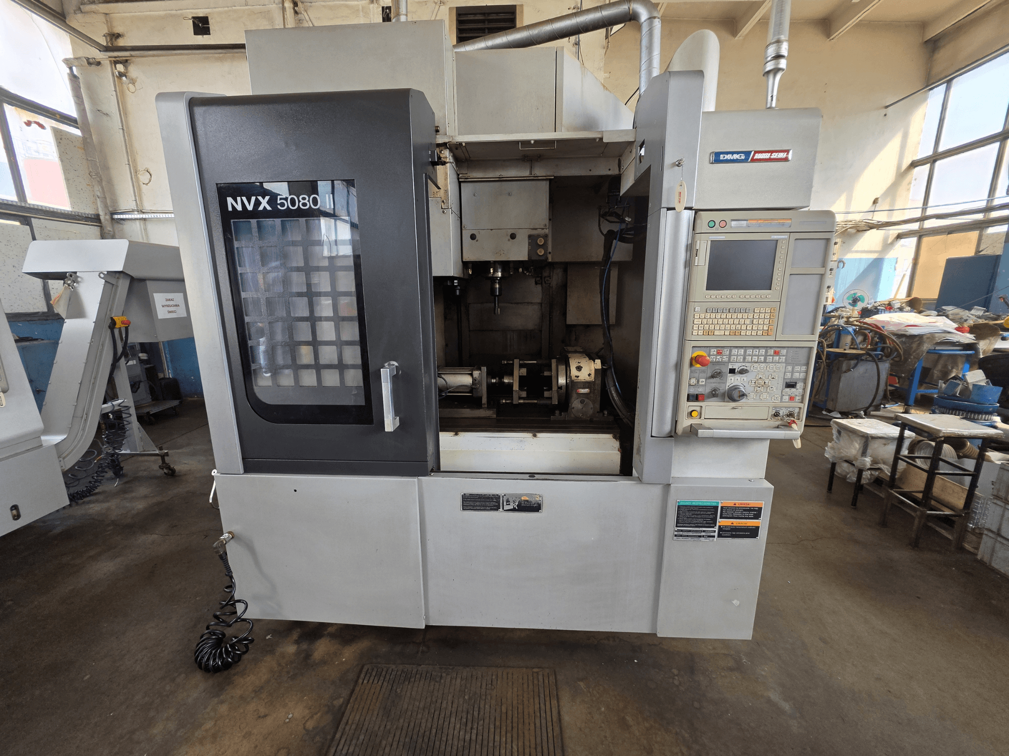 Вигляд спереду вертикального обробного центру DMG Mori Seiki NVX 5080 II/40 з панеллю керування та прозорим вікном, що демонструє зону обробки.