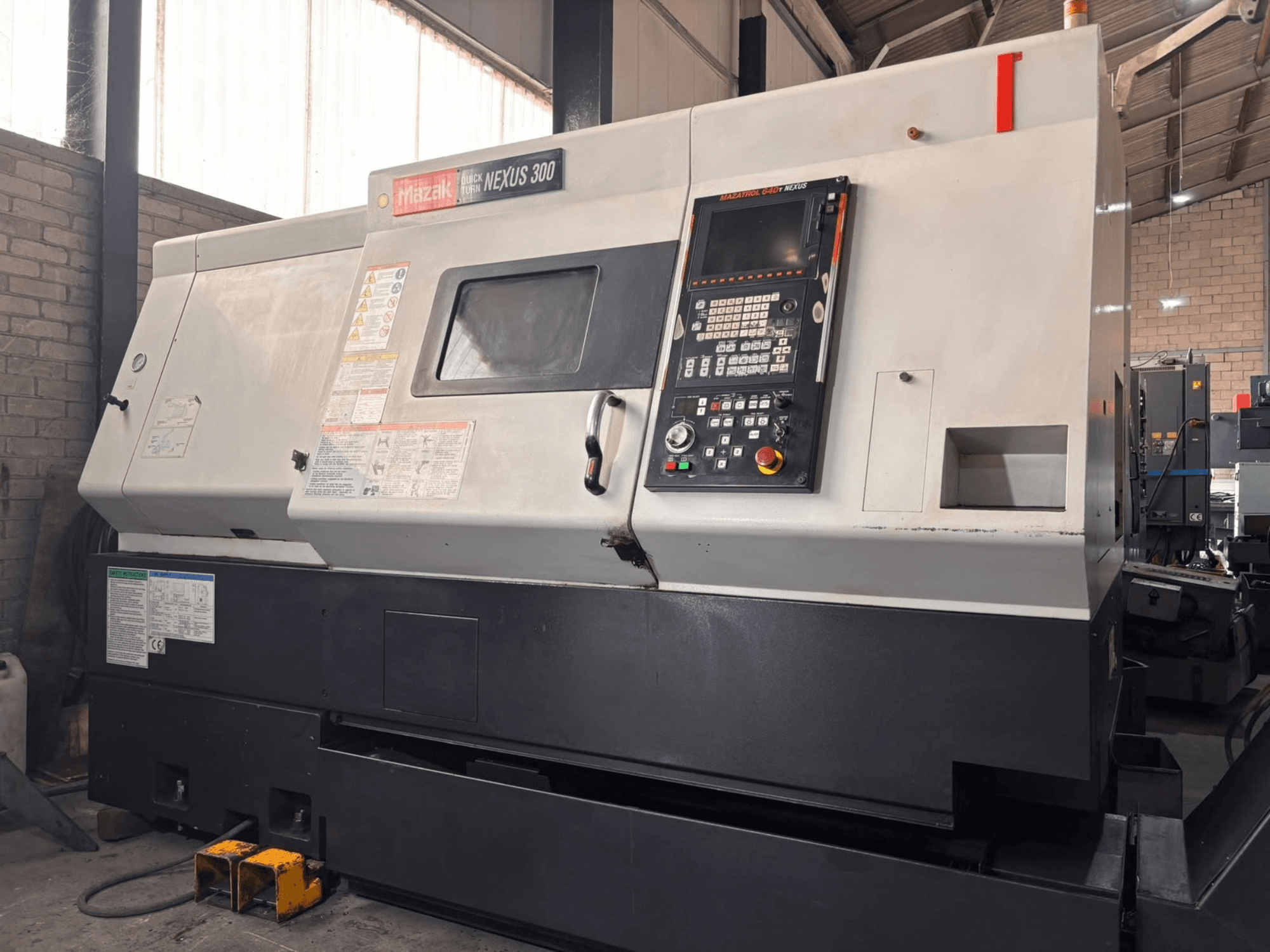 Горизонтальний токарний верстат Mazak QT NEXUS 300, вид збоку, на якому видно панель керування та індикатори роботи в умовах цеху.