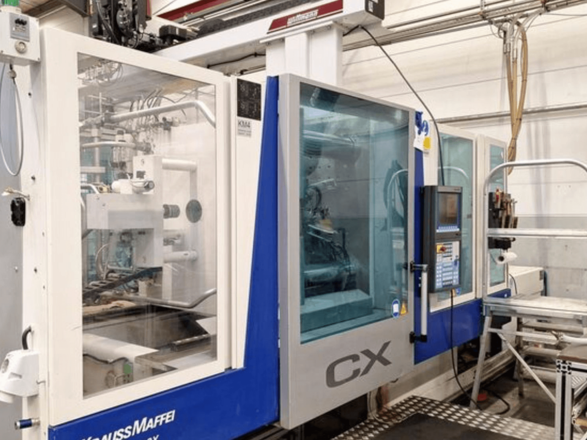 Гідравлічна термопластавтомат Krauss Maffei 300-1400 CX, вид збоку, на якому видно панель управління та прозорий кожух.
