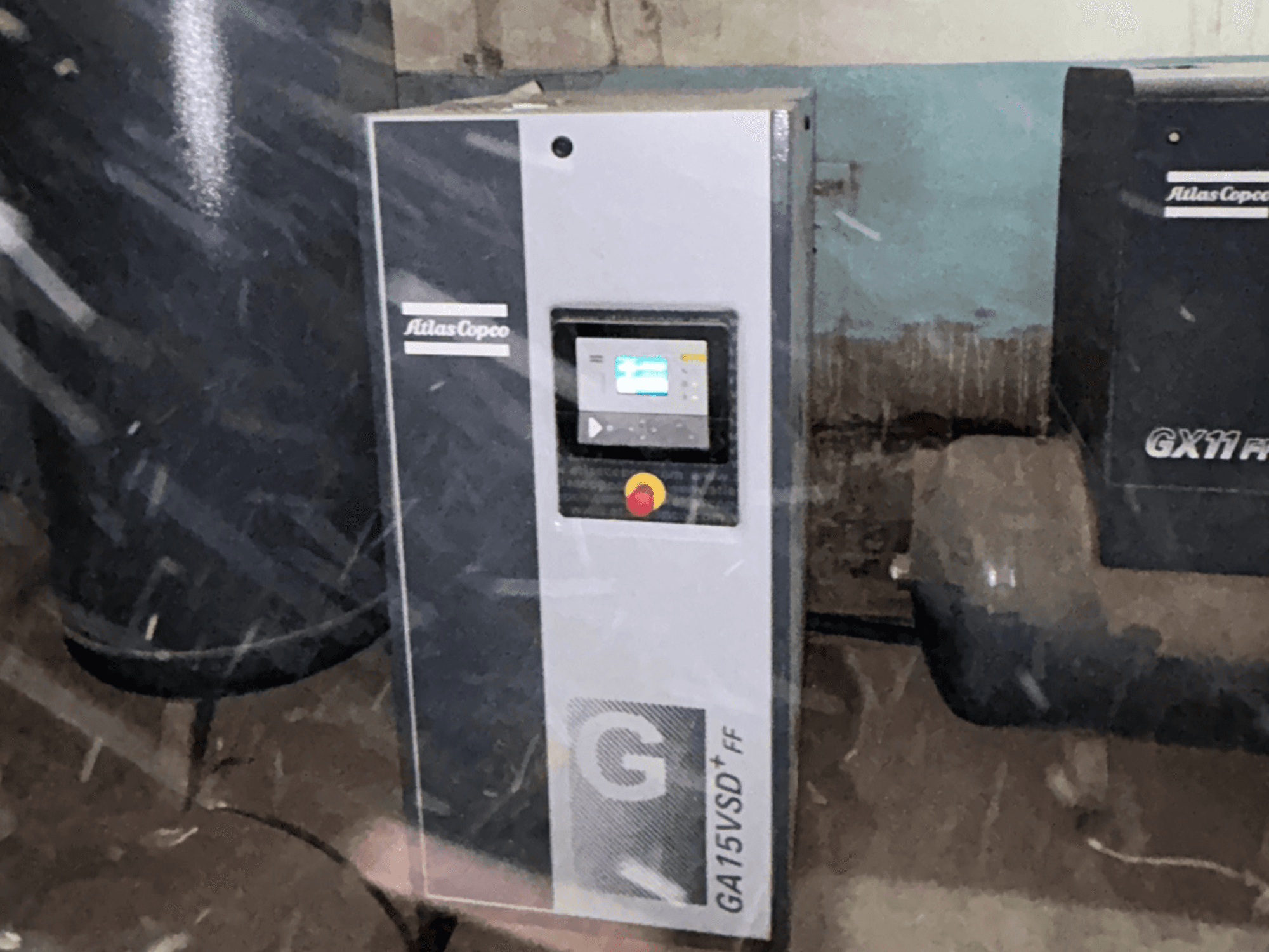 Повітряний компресор Atlas Copco GA15VSD+FF, вид спереду, укомплектований панеллю керування з дисплеєм та червоною кнопкою аварійної зупинки.