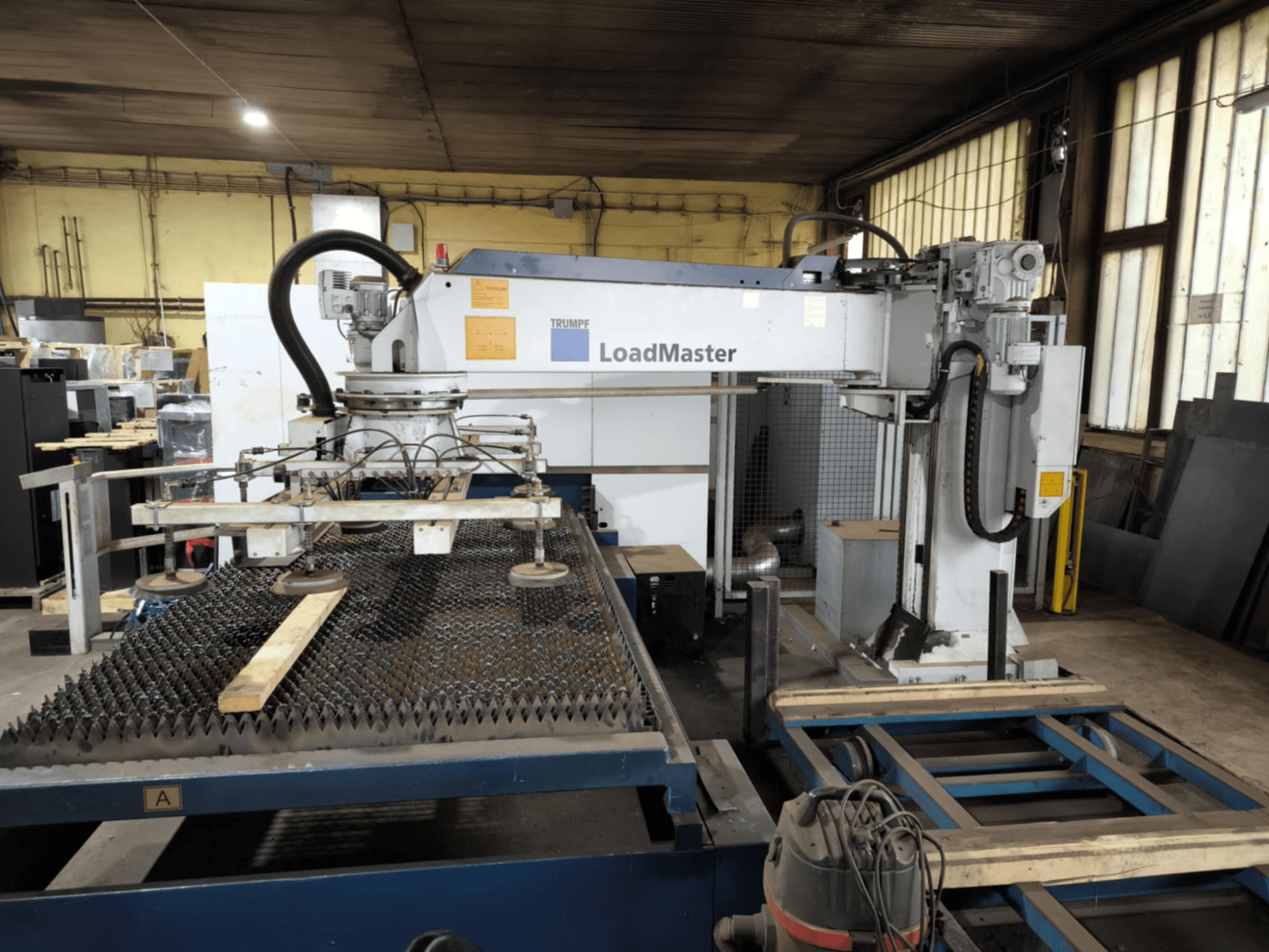 Верстат для різання волокна TRUMPF TRULASER 3030, вид спереду, демонструє систему LoadMaster і розміщений на решітчастому робочому столі.