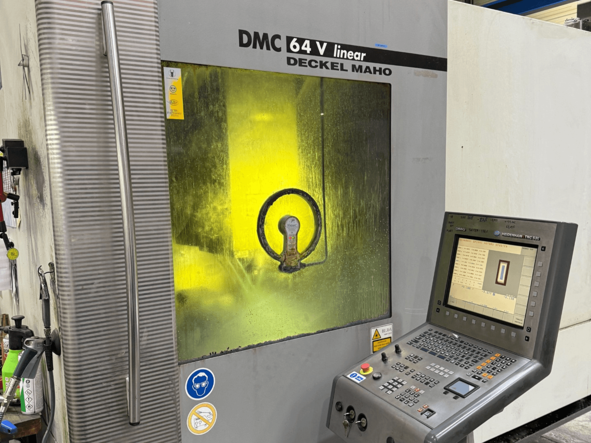 DMC 64 V linear від Deckel Maho, вигляд спереду машини з панеллю керування та жовтим тонованим вікном, що показує внутрішні механізми.