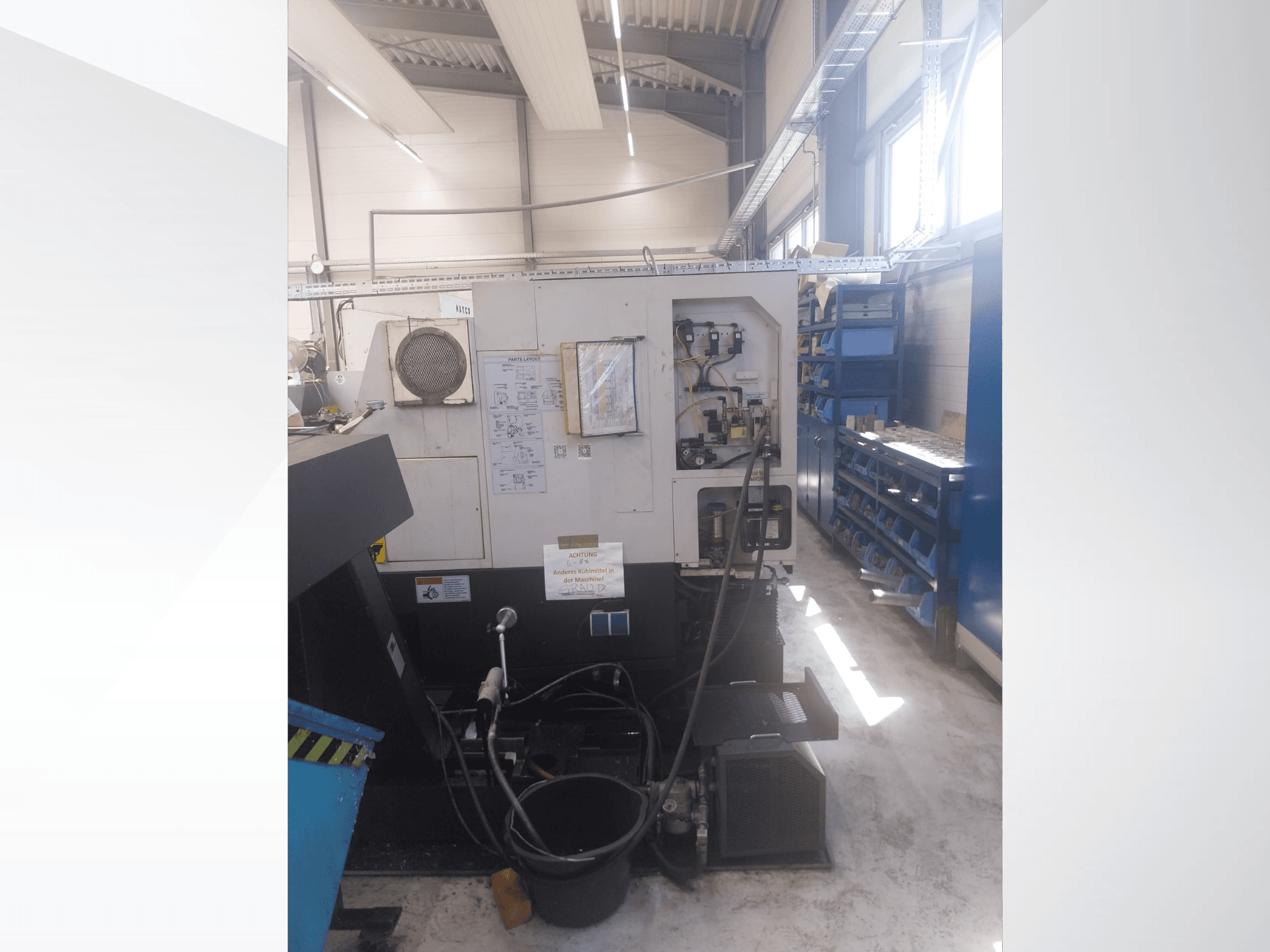 Mazak QUICK TURN NEXUS 200 MS, вид збоку, на якому видно панель управління, шланги та зону розміщення інструментів у цехових умовах.