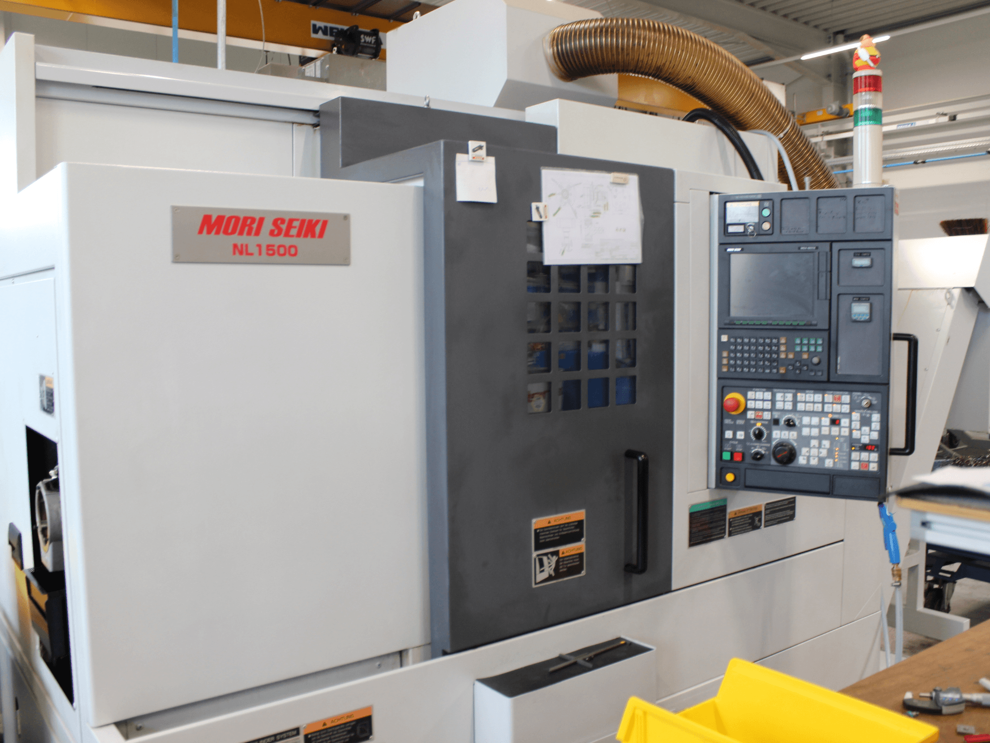 Токарно-фрезерний центр MORI SEIKI NL 1500 SY у боковому ракурсі: на фото зображено панель управління, наклейки з інструкціями щодо техніки безпеки та систему охолодження.