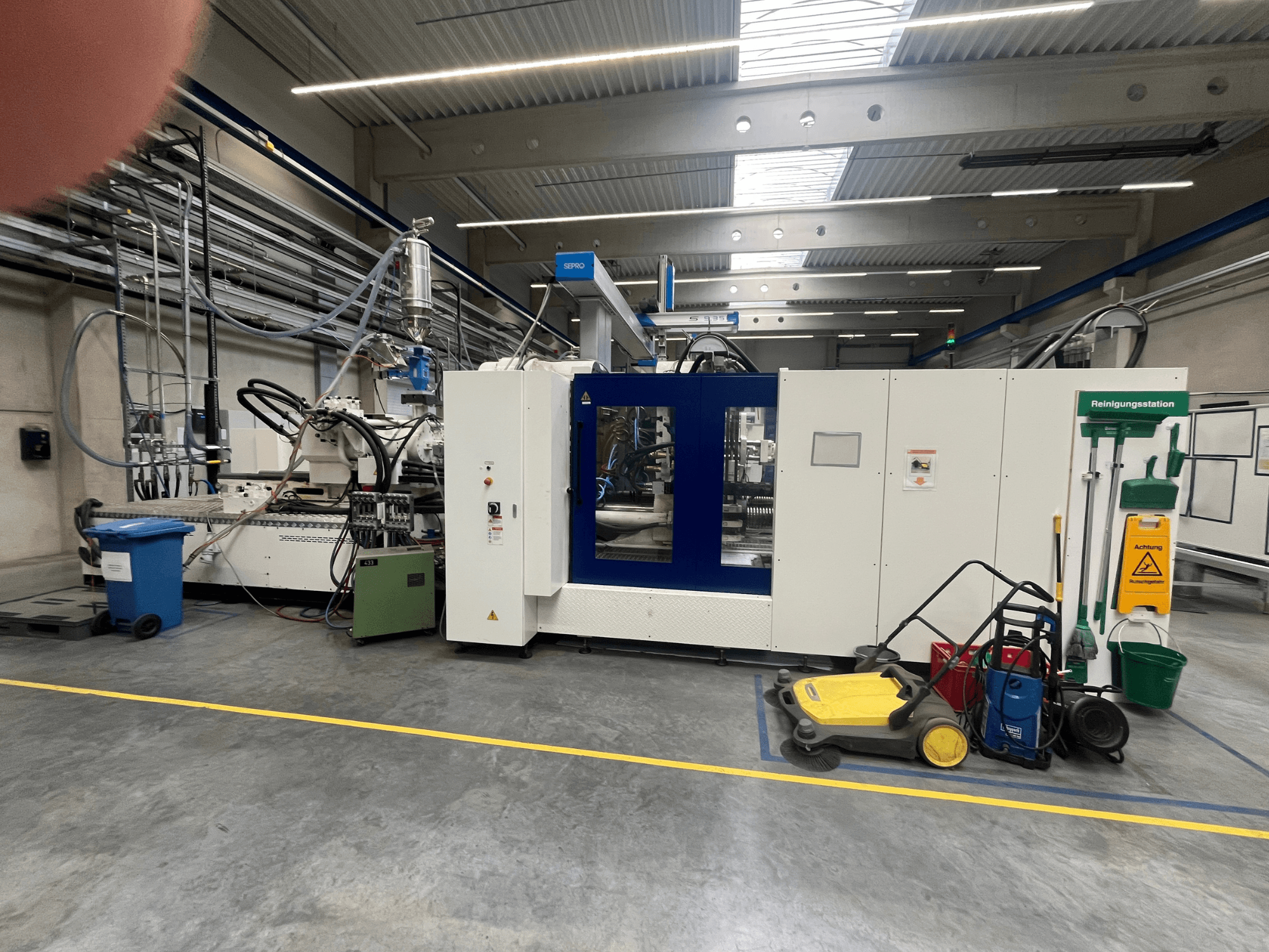 Промислова машина на заводі, вид спереду, з синьо-білими панелями, шлангами та очисним обладнанням поруч.