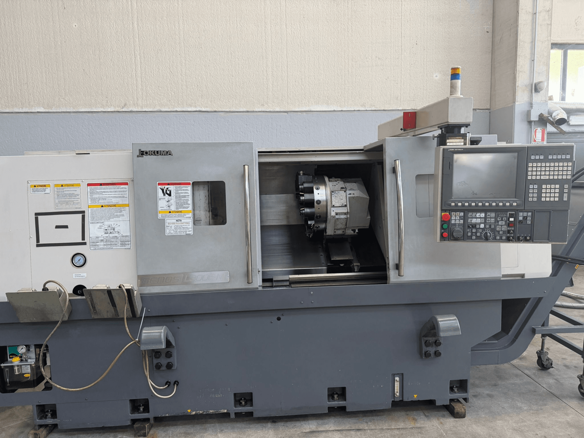 Токарний верстат з ЧПК Okuma, вид спереду, з панеллю керування, тримачем ріжучого інструменту та попередженнями про безпеку збоку.