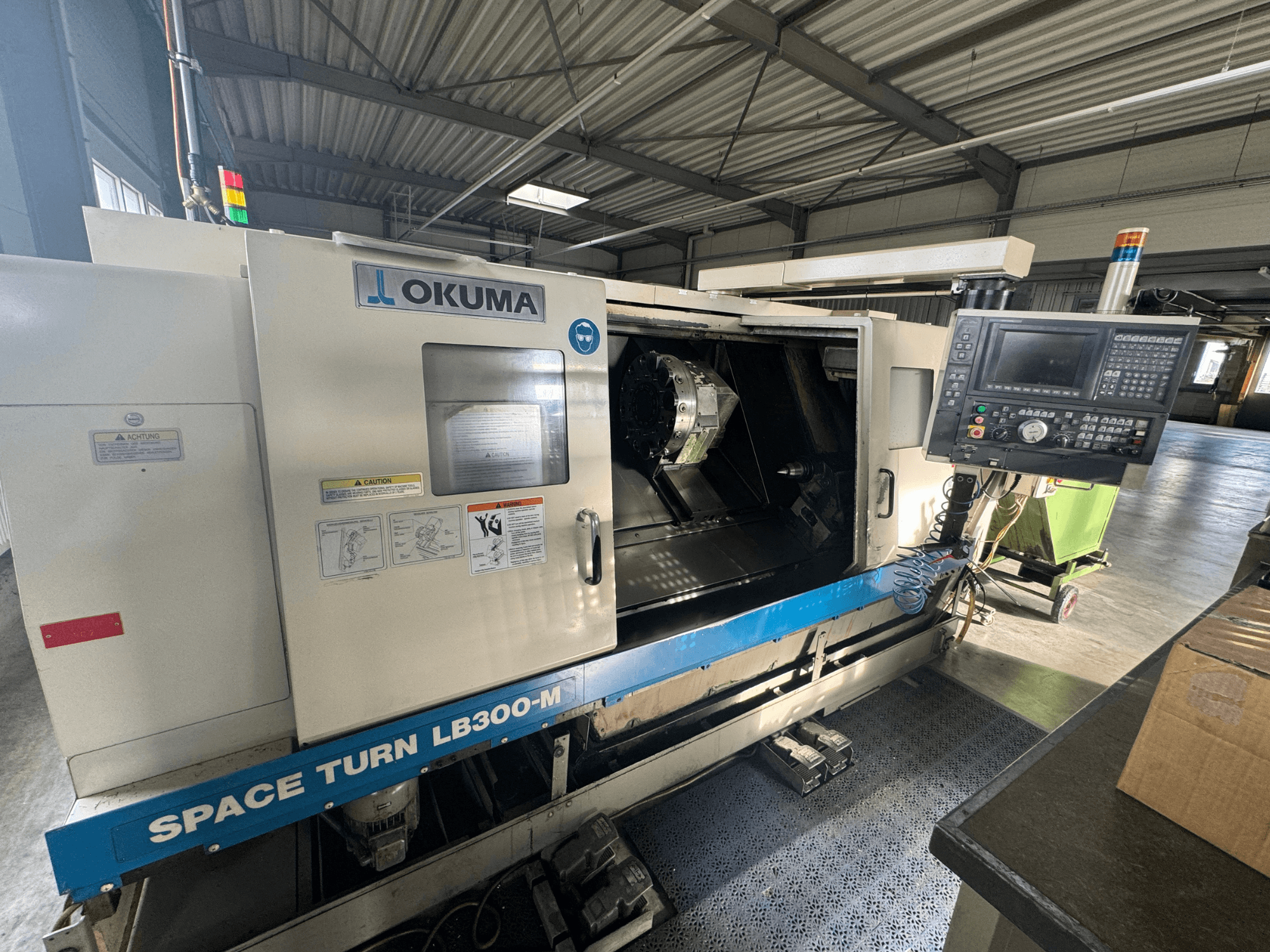 Токарний верстат з ЧПК Okuma Space Turn LB300-M спереду, з панеллю керування та відкритими дверцятами, що відкривають внутрішню зону обробки.