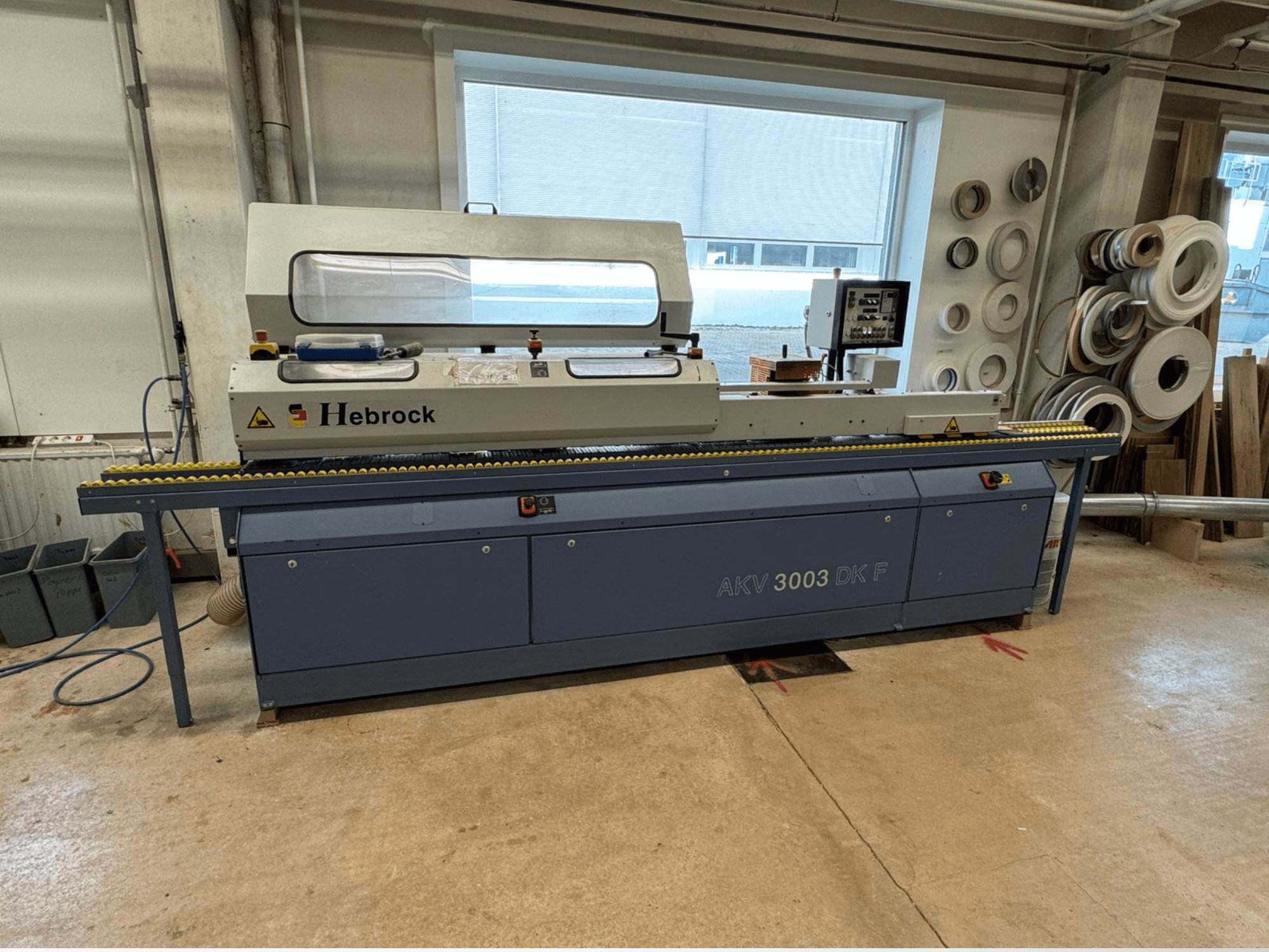 Кромкооблицювальний верстат Hebrock AKV 3003 DK F, вид спереду, з конвеєром і панеллю керування, розташований у майстерні.