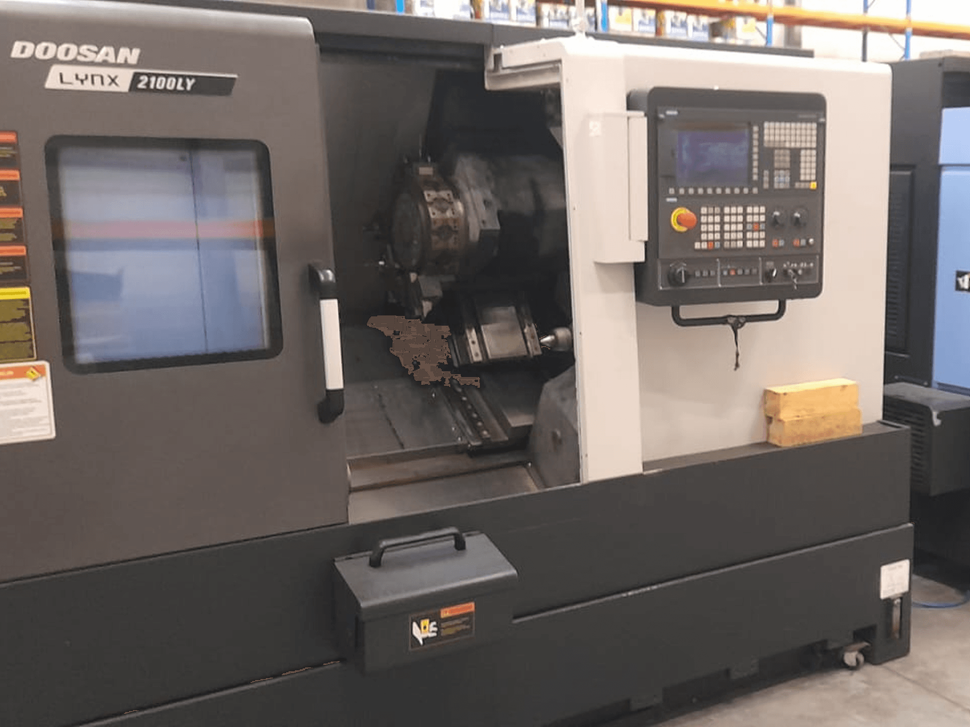 Токарний верстат з ЧПК Doosan Lynx 2100LY, вид спереду: панель керування, тримач інструменту та внутрішній робочий простір; видно технічні етикетки.