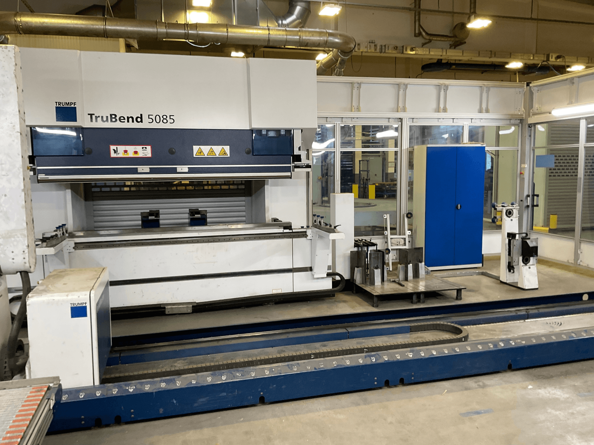 TruBend 5085 від TRUMPF, вид збоку великого металозгинального верстата з панеллю керування та різними інструментами поруч.