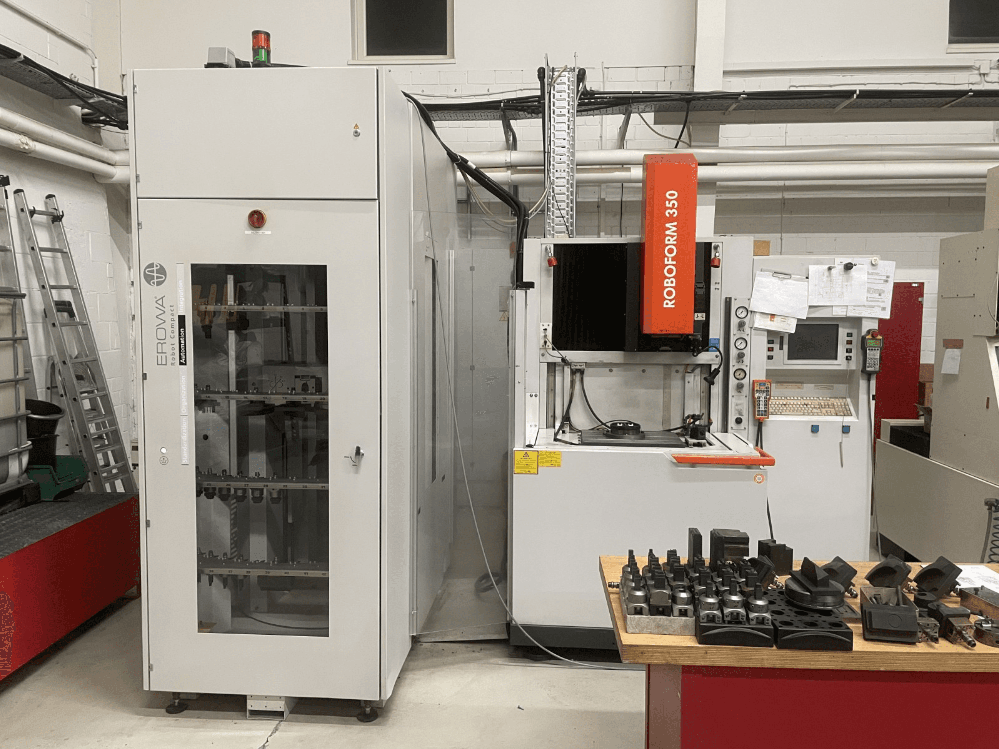 Висікальний електроерозійний верстат CHARMILLES Roboform 350, вид спереду, з інструментами, розміщеними на столі, та суміжним обладнанням.