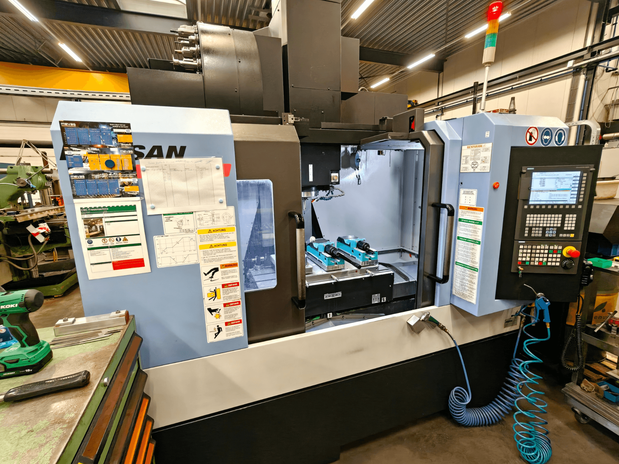 Вертикальний обробний центр DOOSAN DNM 400 II в майстерні, з органами керування, тримачами інструментів та знаками безпеки, вид спереду.