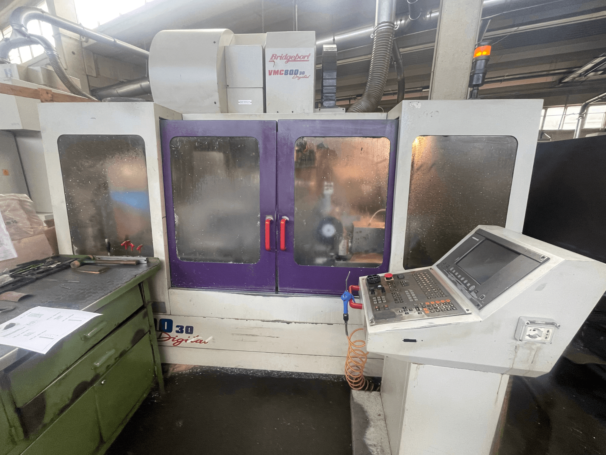 Вертикальний обробний центр Bridgeport VMC 800/30, вид спереду, на якому видно панель управління та фіолетові дверцята, а також інструменти на сусідній поверхні.