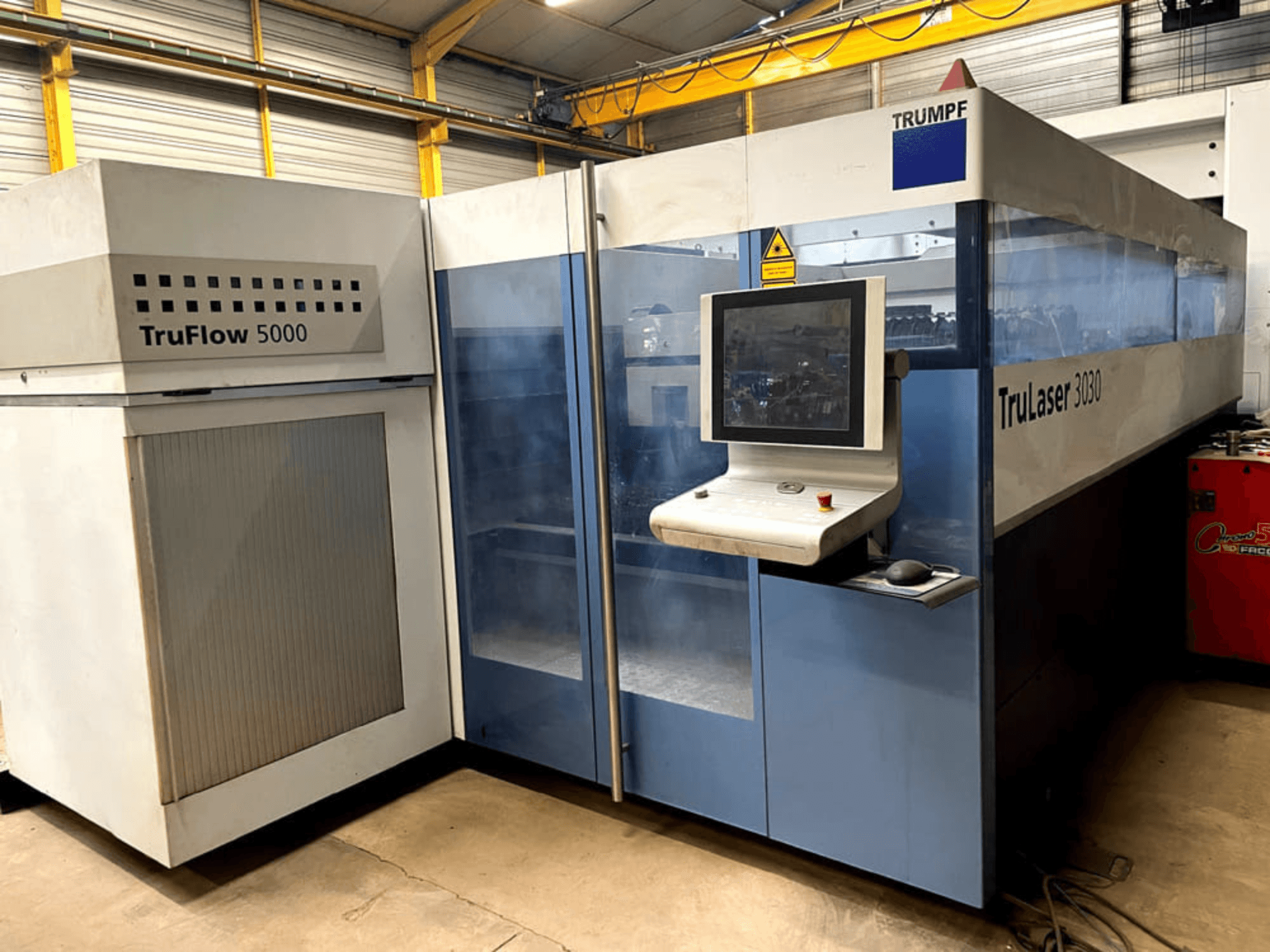 Лазерний верстат для різання CO2 TRUMPF TruLaser 3030 у фронтальному ракурсі, з панеллю керування та сусіднім блоком TruFlow 5000.