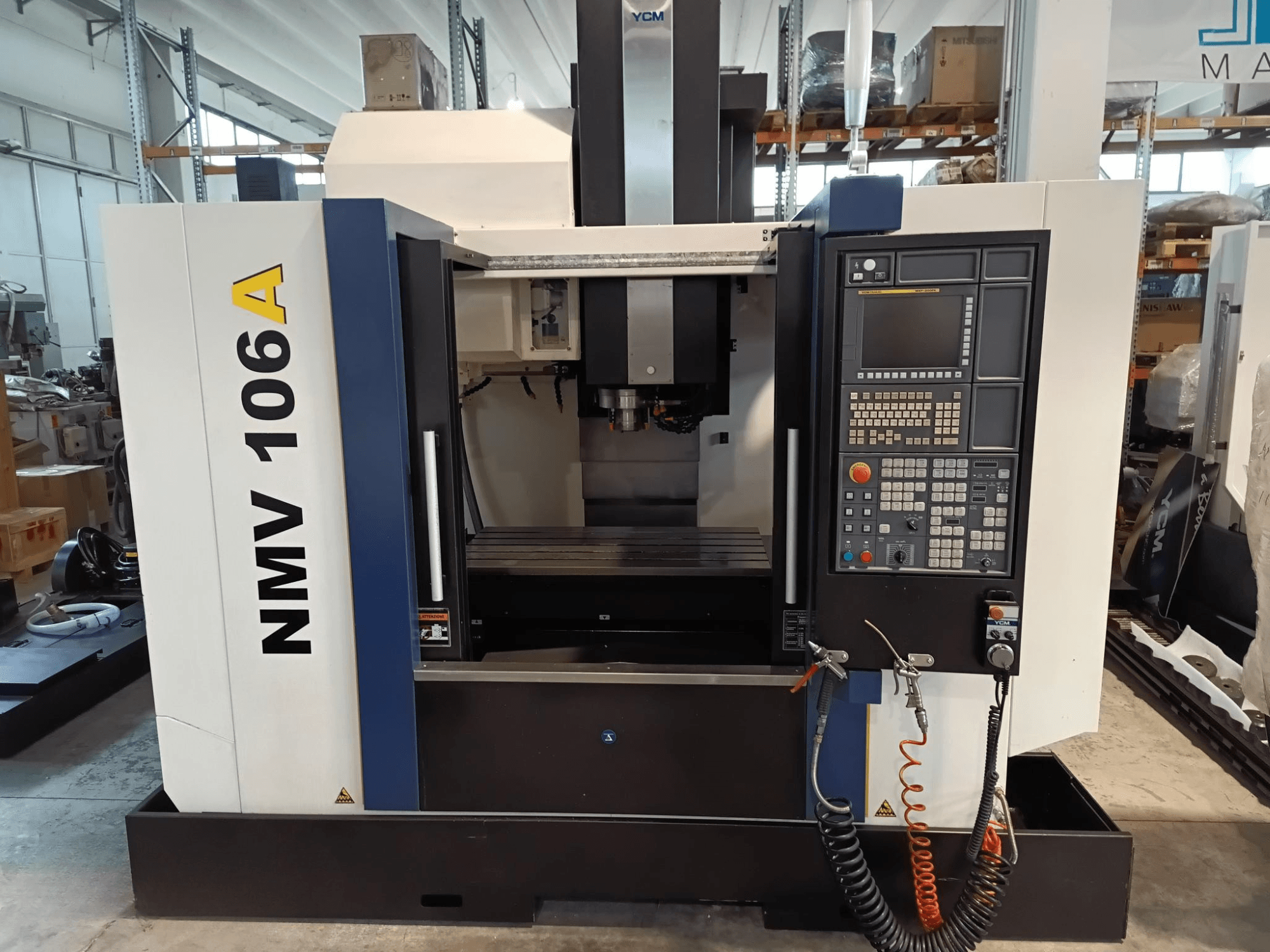 Обробний центр YCM NMV 106A, вид спереду, з панеллю керування з кнопками та шлангами для ЗОР.