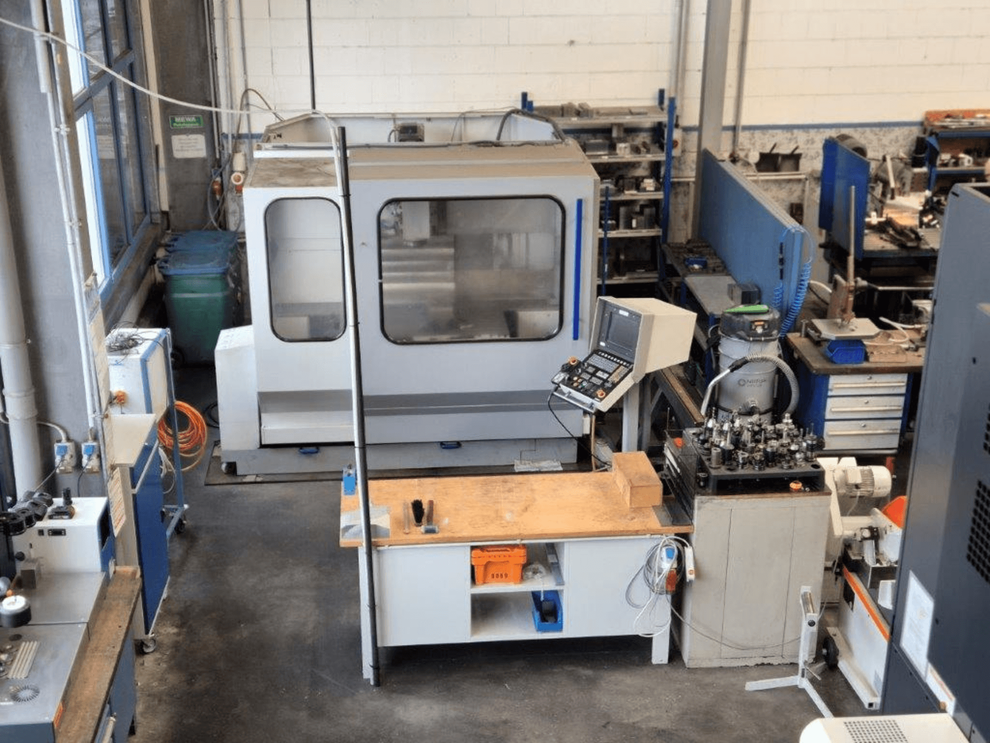 Фрезерний верстат з ЧПУ в майстерні, вид спереду, з панеллю керування, робочою поверхнею та інструментами на задньому плані.