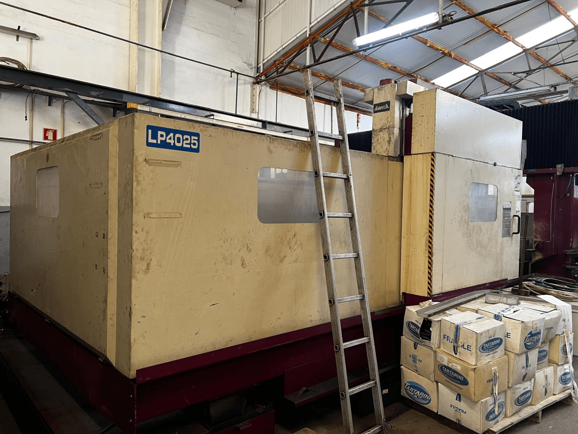 Портальний фрезерний верстат AWEA LP4025 у промисловому приміщенні; вид збоку, на якому видно велике обладнання та ящики для зберігання.