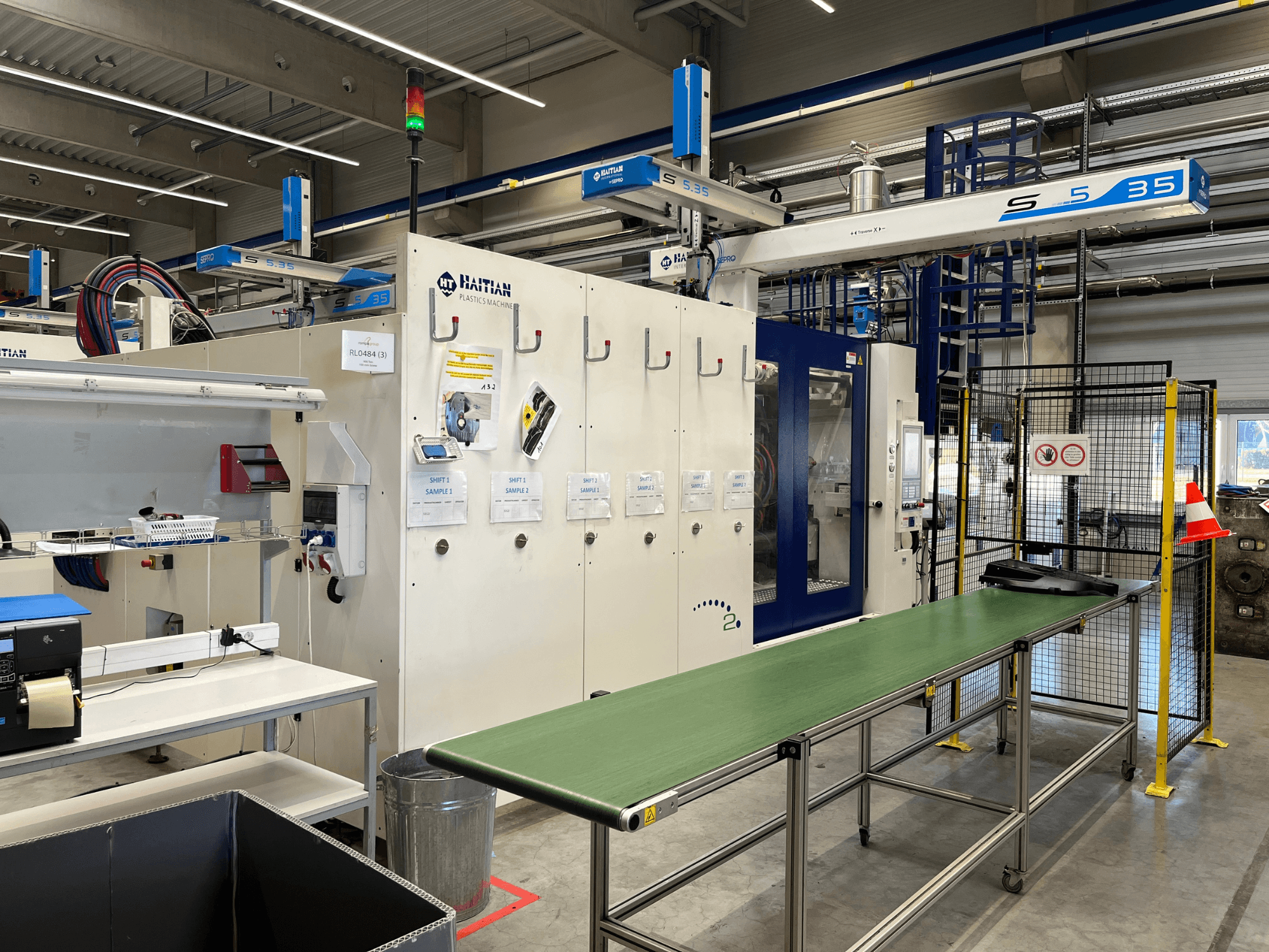 Машина для виготовлення пластмасових виробів Haitian S5-35 у майстерні; зелений стіл конвеєра, захисні бар'єри та панель керування видно спереду.