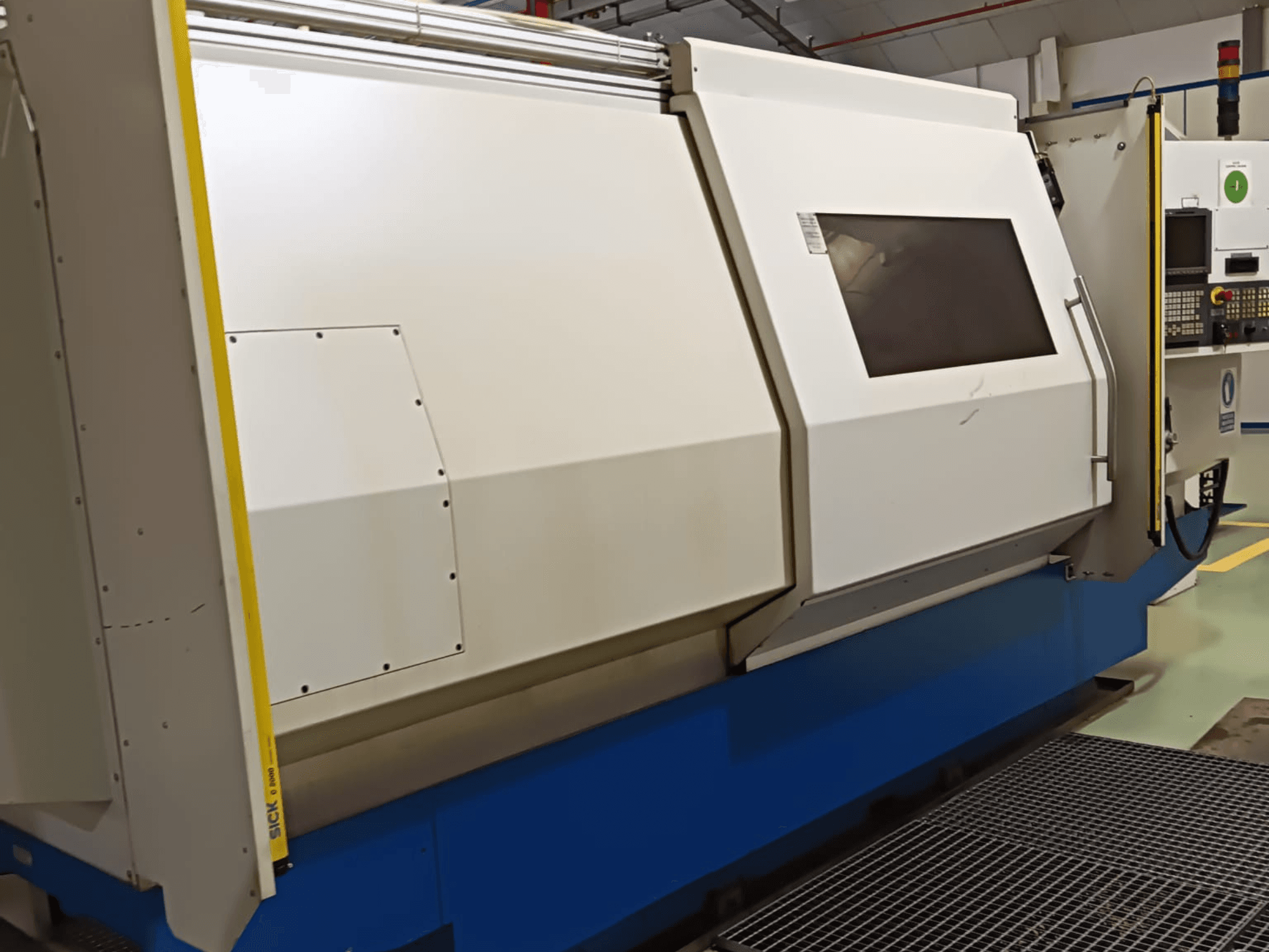 Промисловий токарний верстат, вид збоку, з великим біло-синім корпусом, цифровою панеллю керування та функціями безпеки.