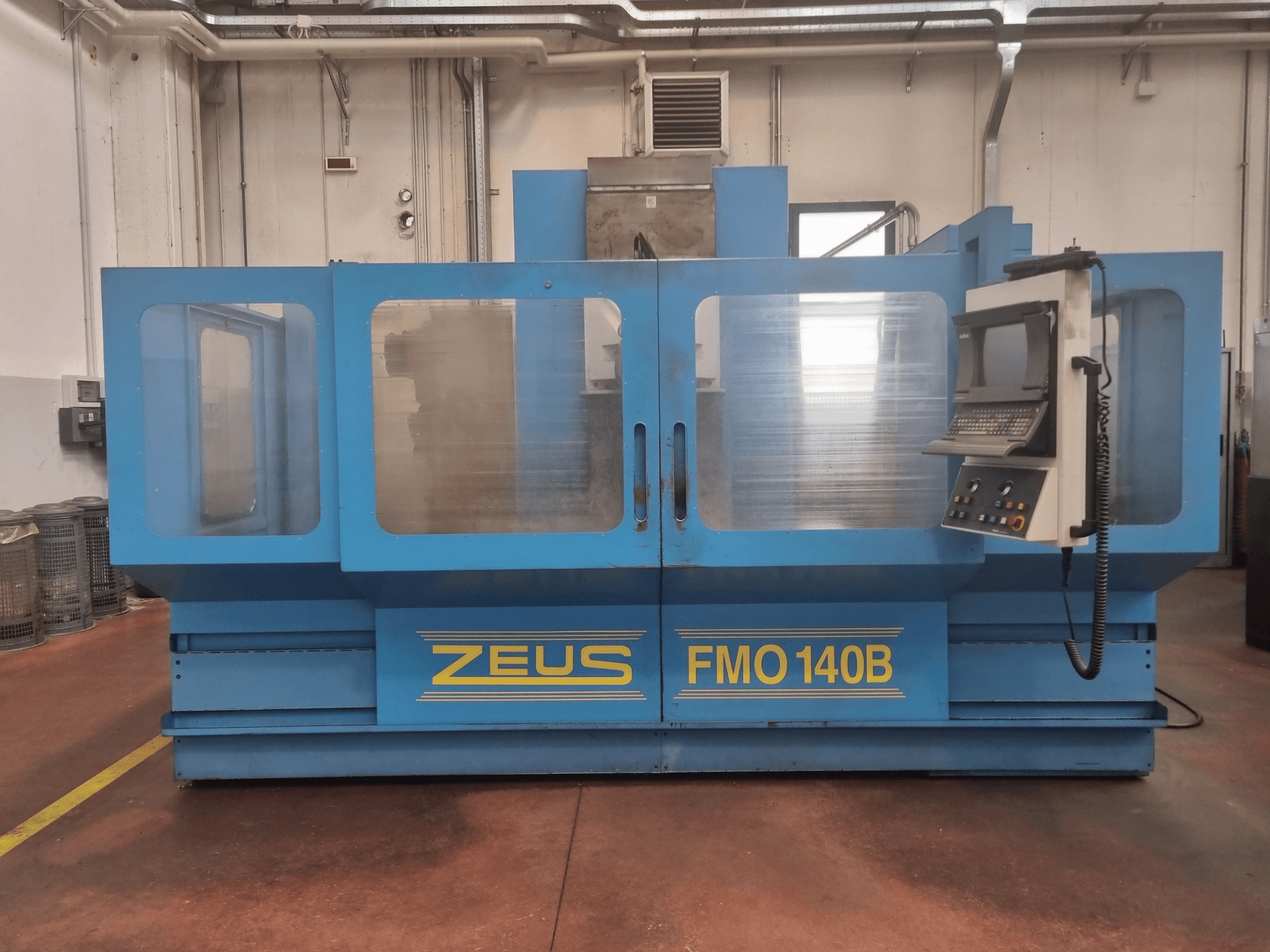 Машина Zeus FMO 140B синього кольору, вид спереду; оснащена панеллю керування та великими прозорими панелями для видимості.