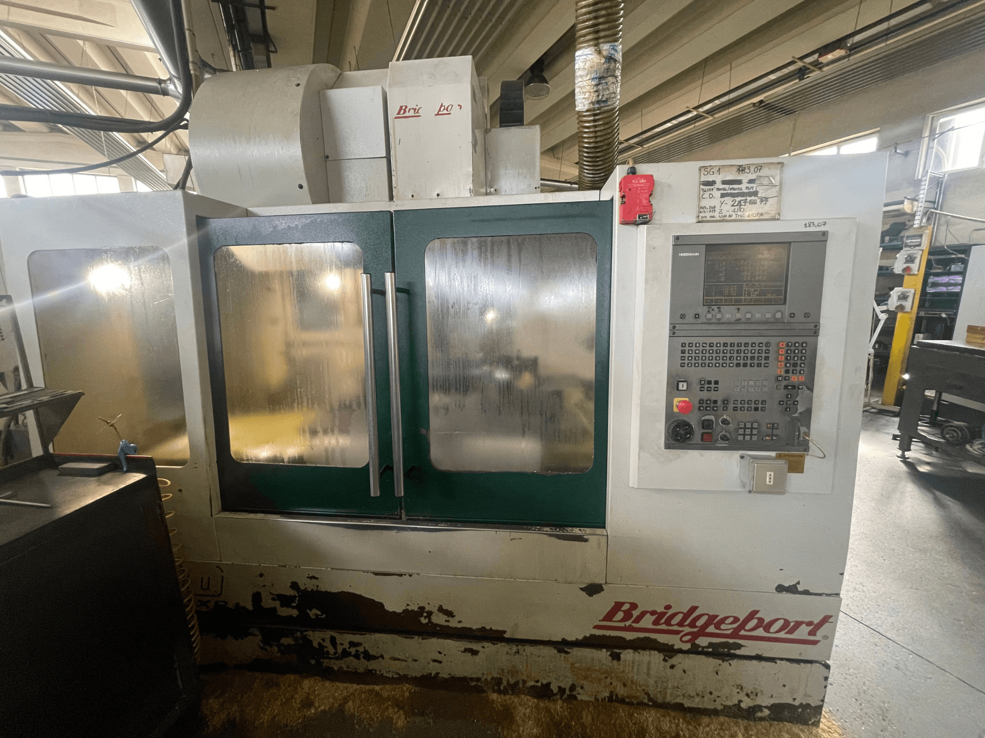 Вертикальний обробний центр Bridgeport VMC 1000/30, вид спереду з панеллю керування; видно зношений зовнішній вигляд та зелені дверцята.