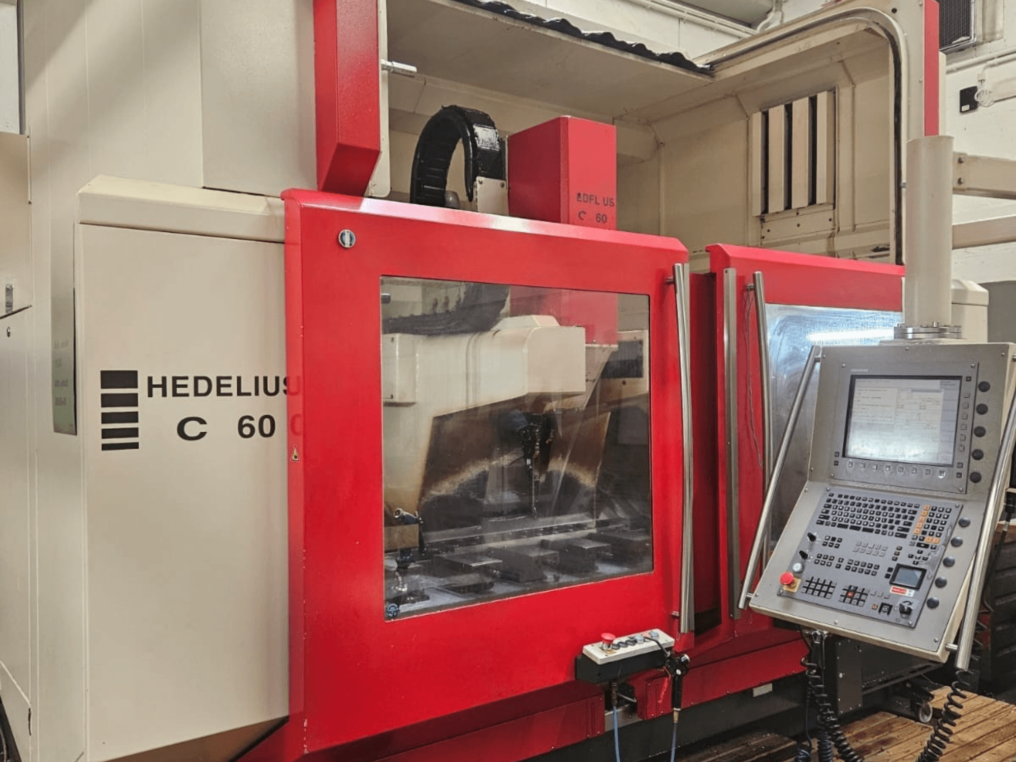 Вертикальний обробний центр HEDELIUS C60 збоку, з червоною передньою панеллю та консоллю керування з дисплеєм.