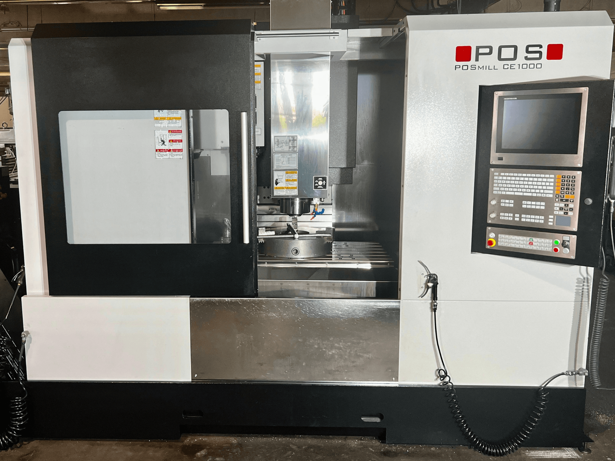 Вигляд спереду вертикального обробного центру POSmill CE1000, на якому видно панель управління, вікно та металеві поверхні.