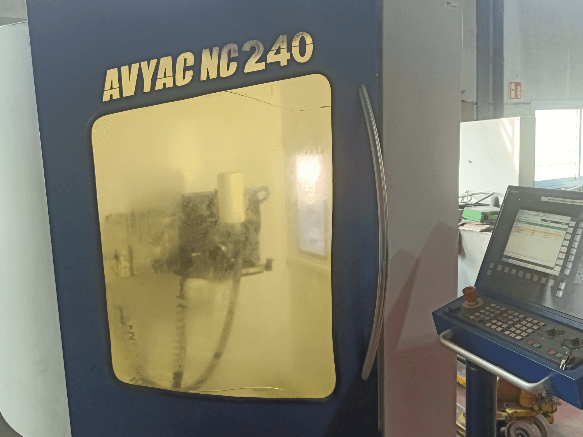 Круглошліфувальний верстат AVYAC NC240, вид збоку з панеллю керування та частково видимою через вікно зоною шліфування.