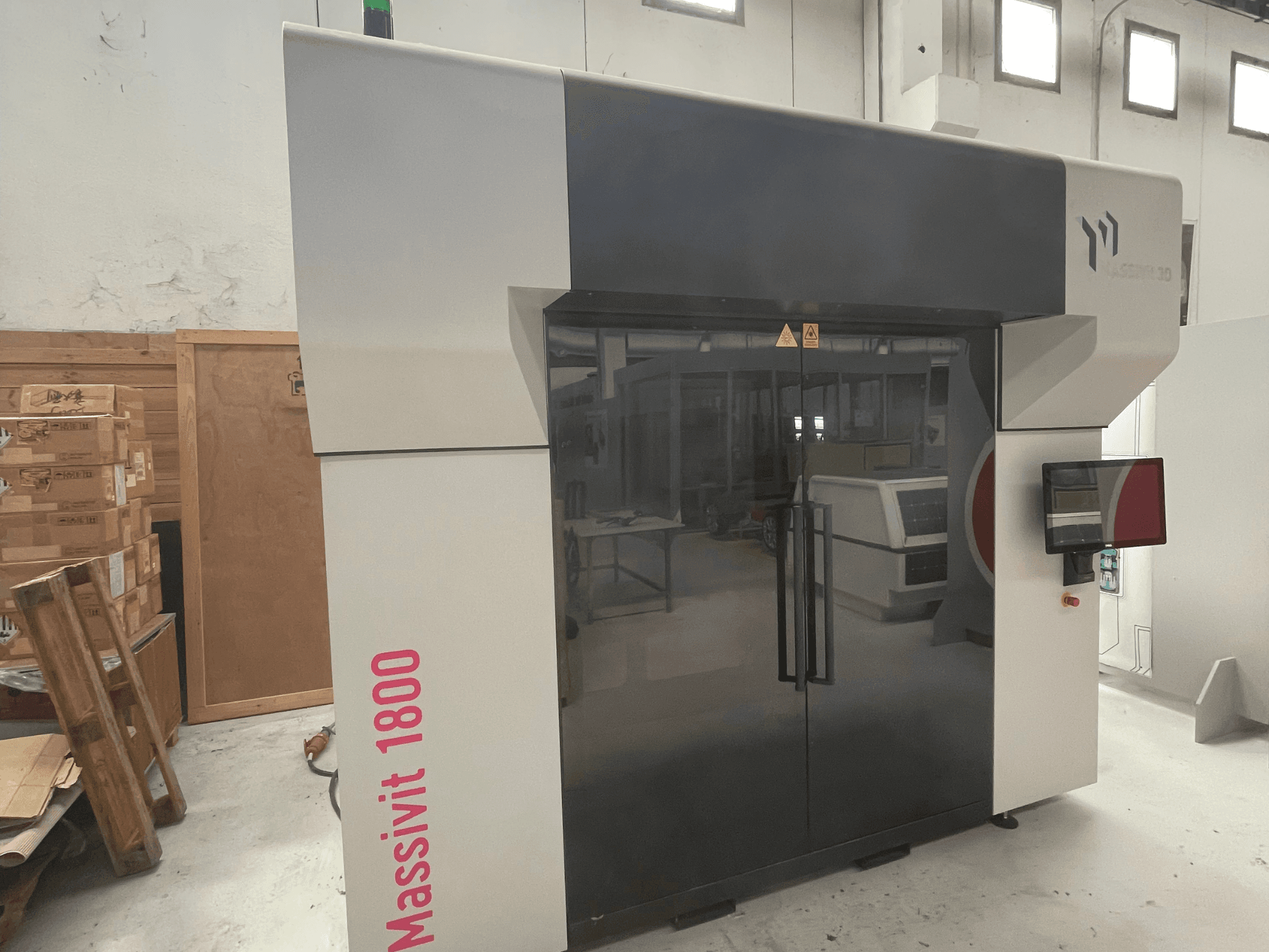 3D-принтер для друку з пластику MASSIVIT Massivit 1800, зображений у бічному ракурсі, оснащений сенсорним екраном та має елегантний чорно-білий дизайн.
