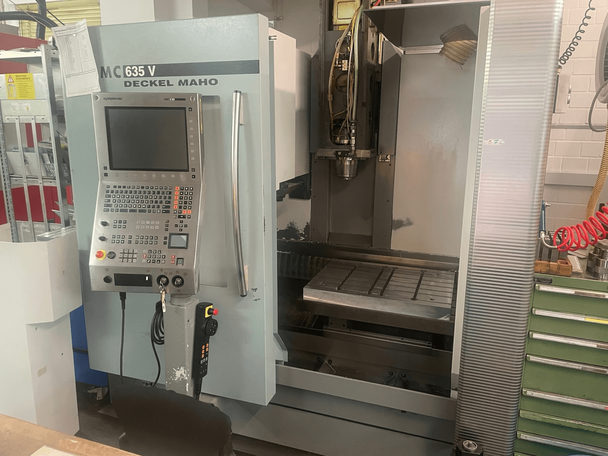 Вигляд спереду вертикального обробного центру DECKEL MAHO DMC 635 V з панеллю керування та відкритою робочою зоною, на якому видно інструментальну головку та станину.