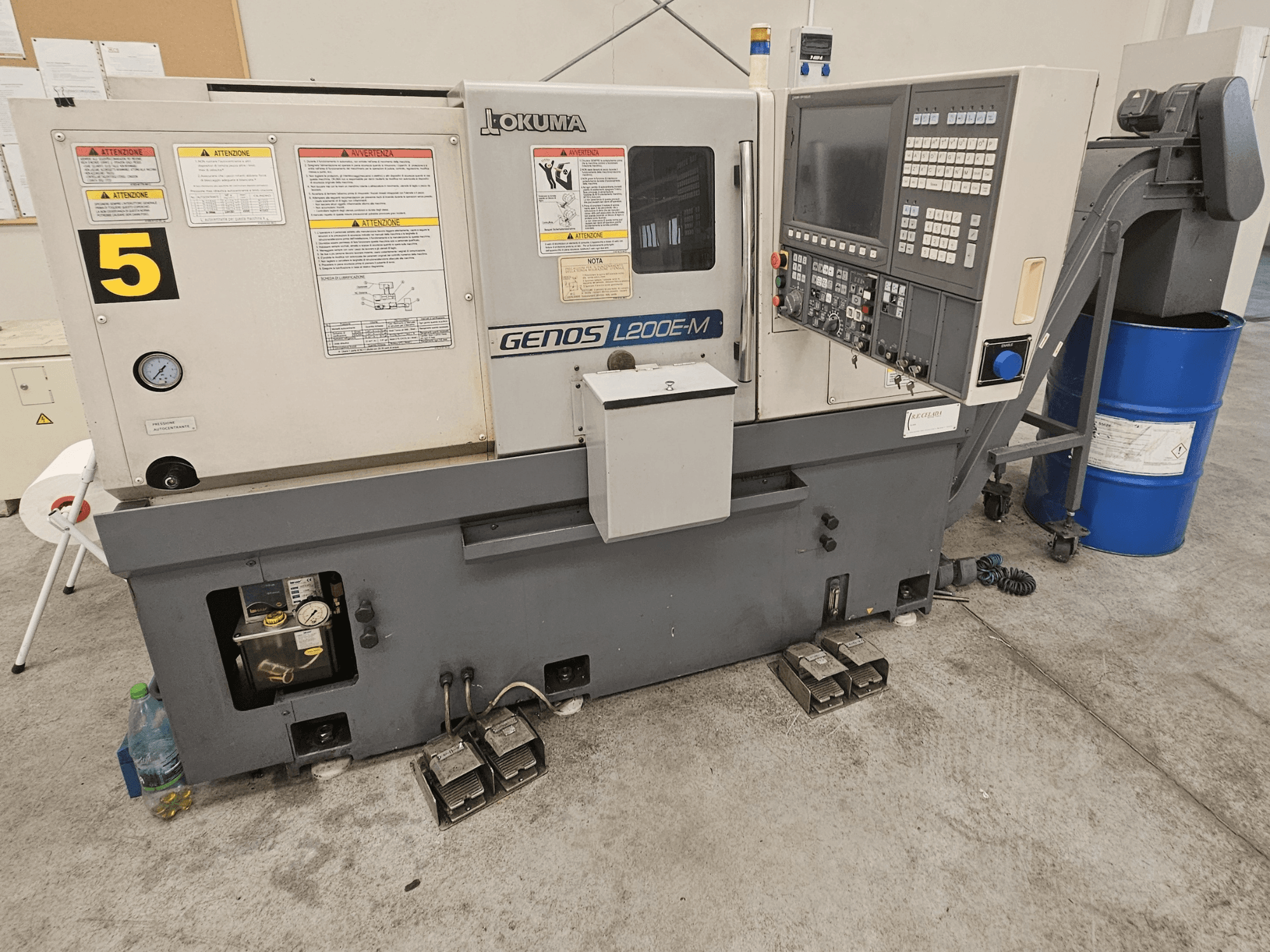 Горизонтальний токарний верстат Okuma GENOS L200E-M, вид спереду, з панеллю керування, етикетками та бачком для ЗОР.