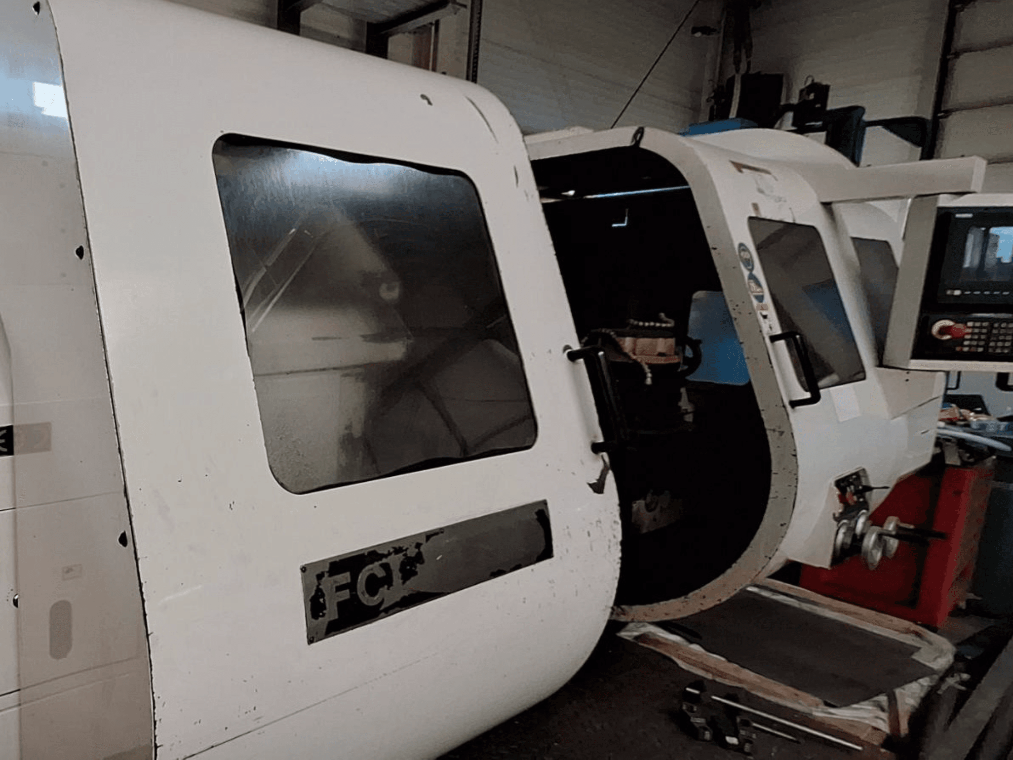 Білий верстат з ЧПУ з видимою панеллю керування та відкритими дверцятами, що демонструють внутрішні компоненти; вигляд спереду. Бренд: FCT.