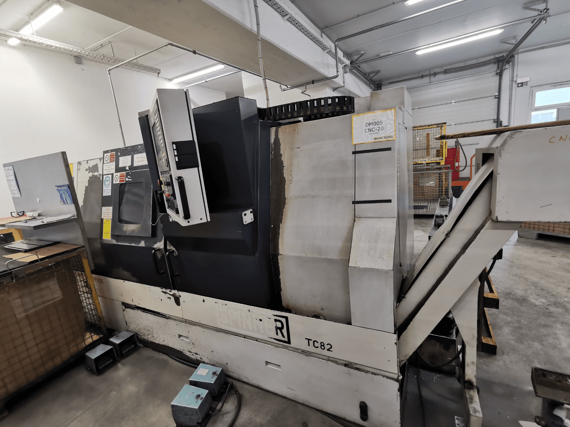 Верстат з ЧПК марки Spinner, модель TC82, вид збоку з панеллю керування та жолобом для видалення брухту в умовах майстерні.