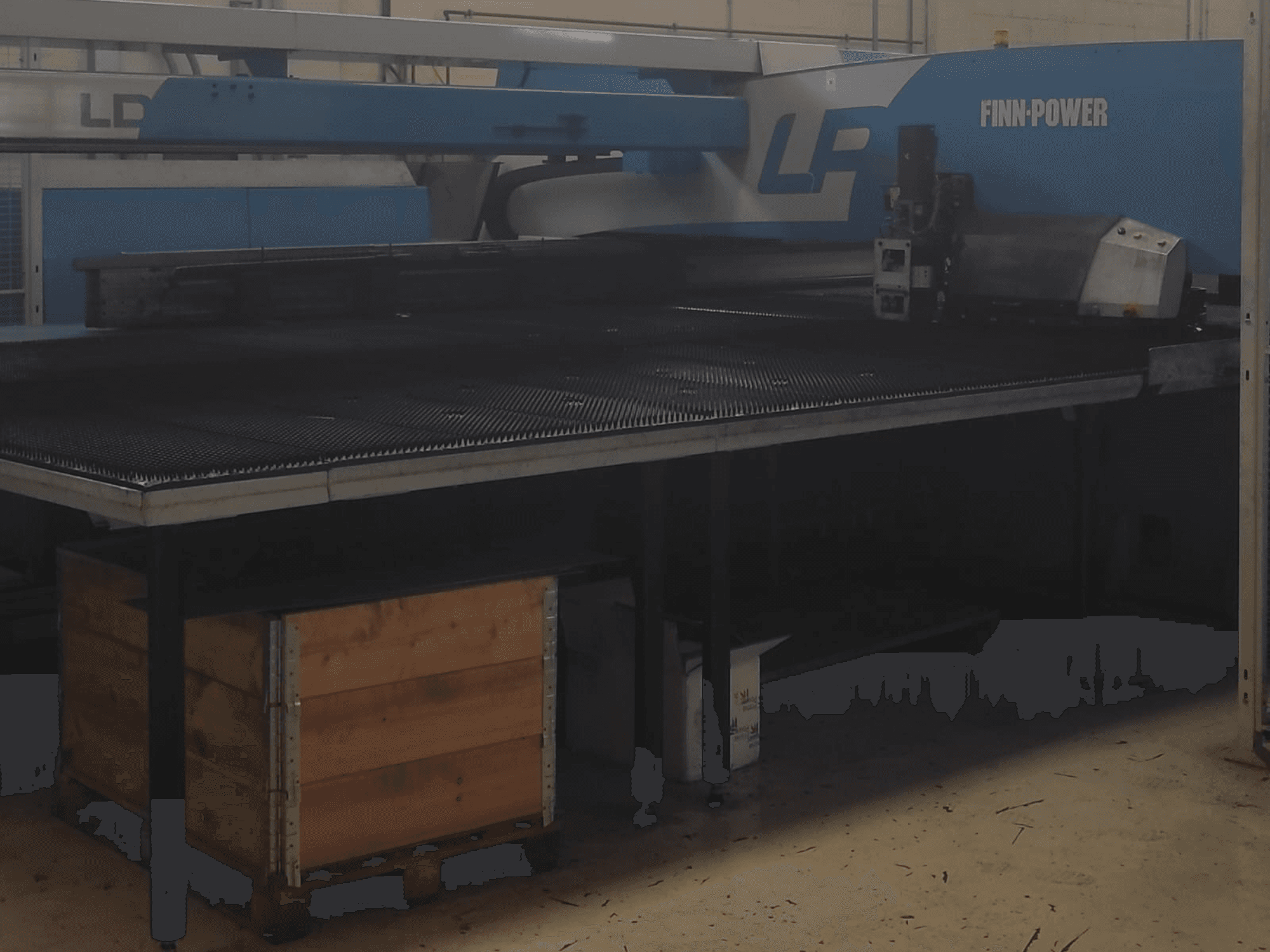 Розкрійний верстат Finn-Power LP на заводі, вид спереду з текстурним металевим столом і дерев'яним ящиком під ним.