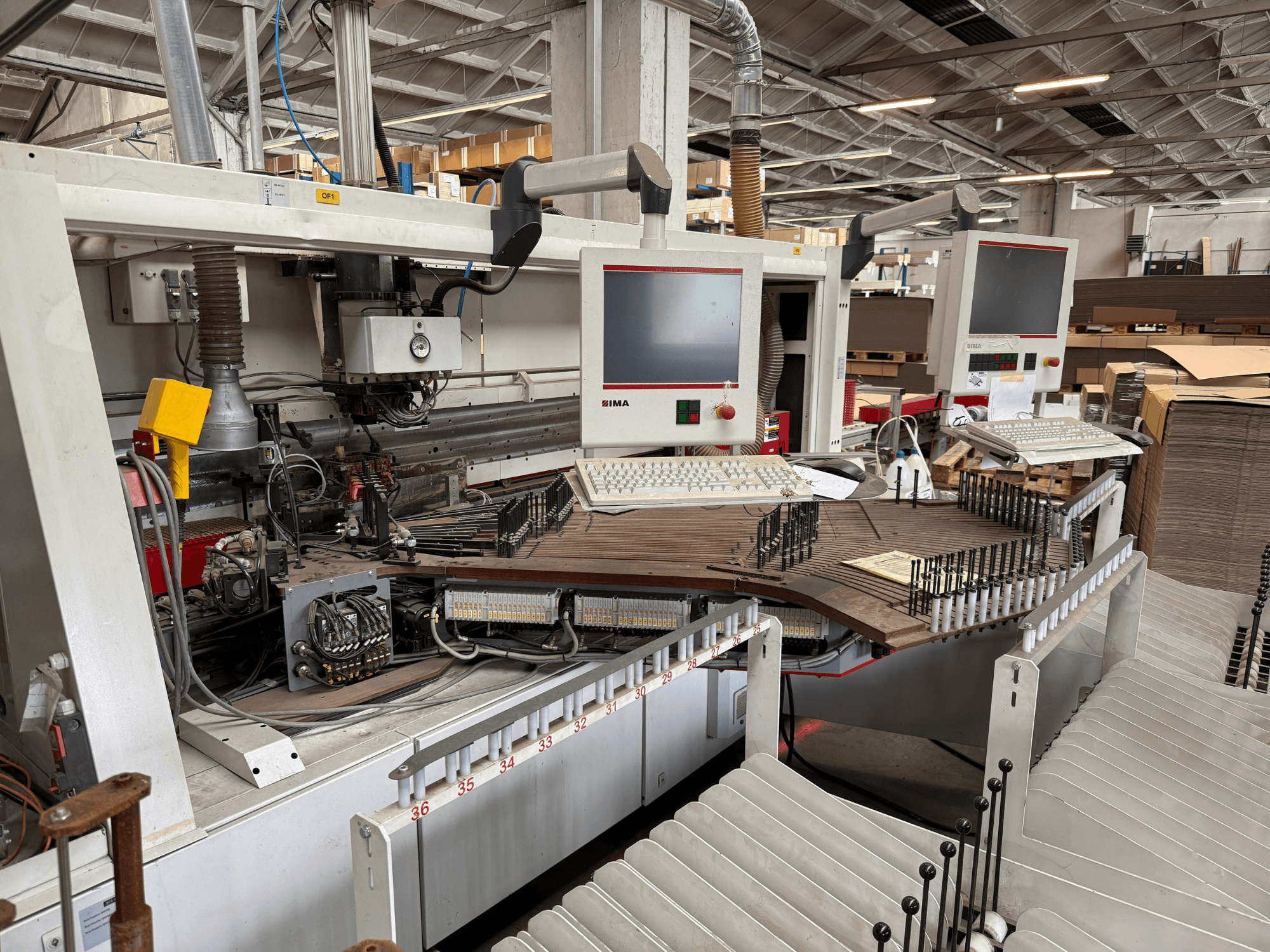 Точний деревообробний верстат IMA з двома моніторами та панелями керування, вид спереду з конвеєром та зоною оснащення.