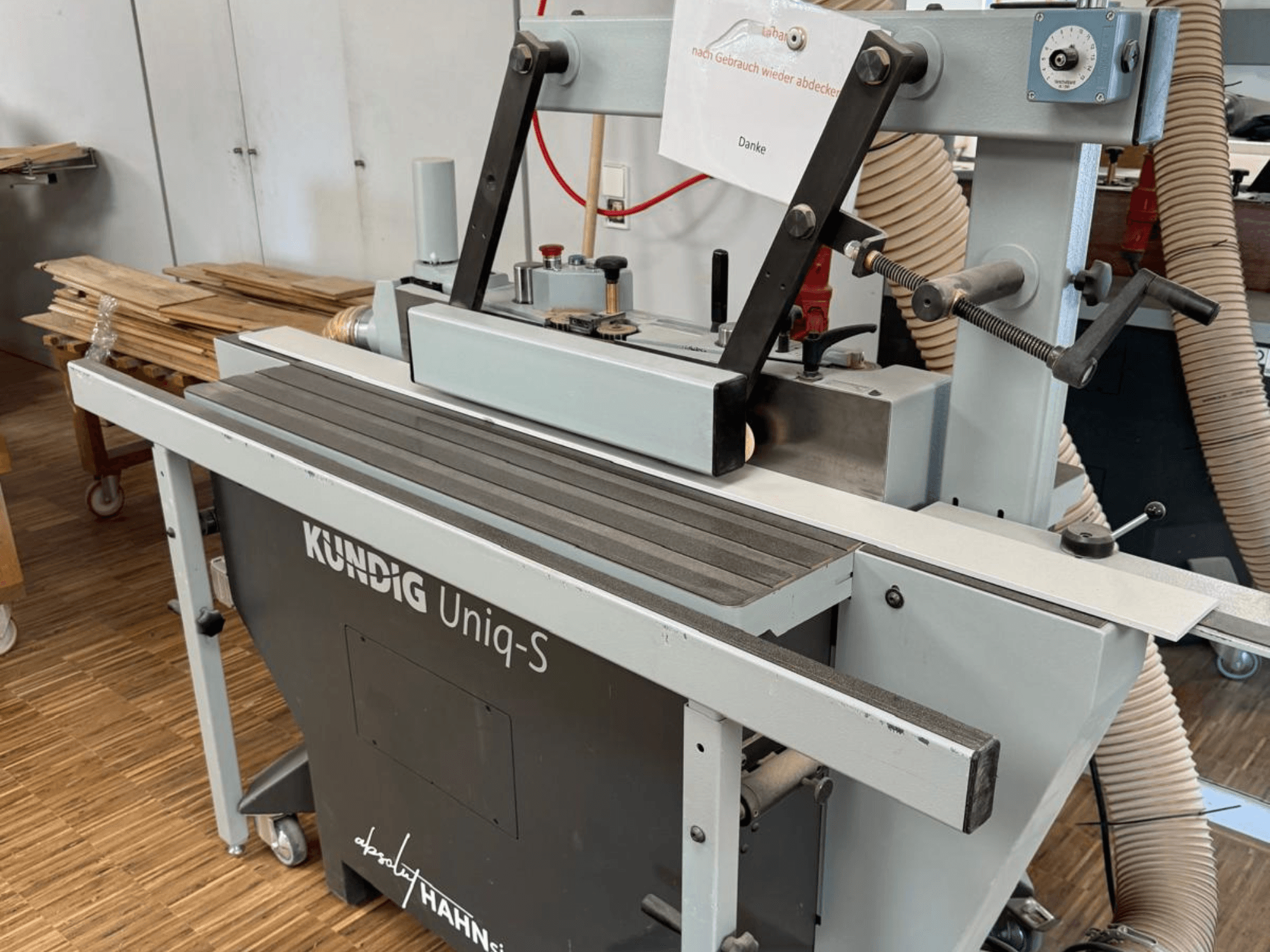Стрічкова шліфувальна машина Kundig UNIQ-S в майстерні, вид збоку, демонструє шліфувальну стрічку та регульовані опорні кронштейни.
